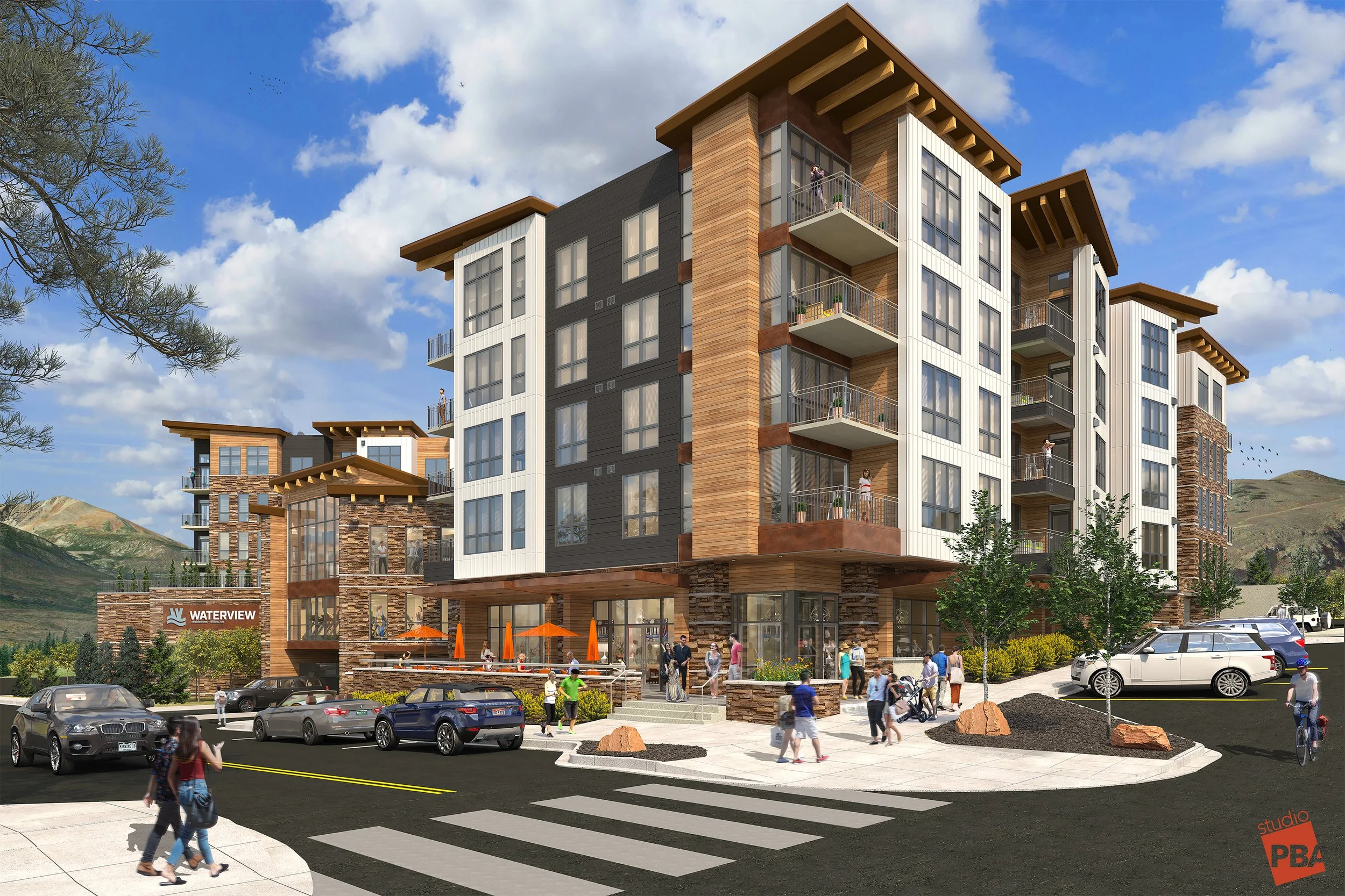 A modern multi-story apartment building with a brick and wood exterior, large windows, and balconies, surrounded by a parking lot and a busy sidewalk with people walking, some crossing a crosswalk, and cars parked and driving.