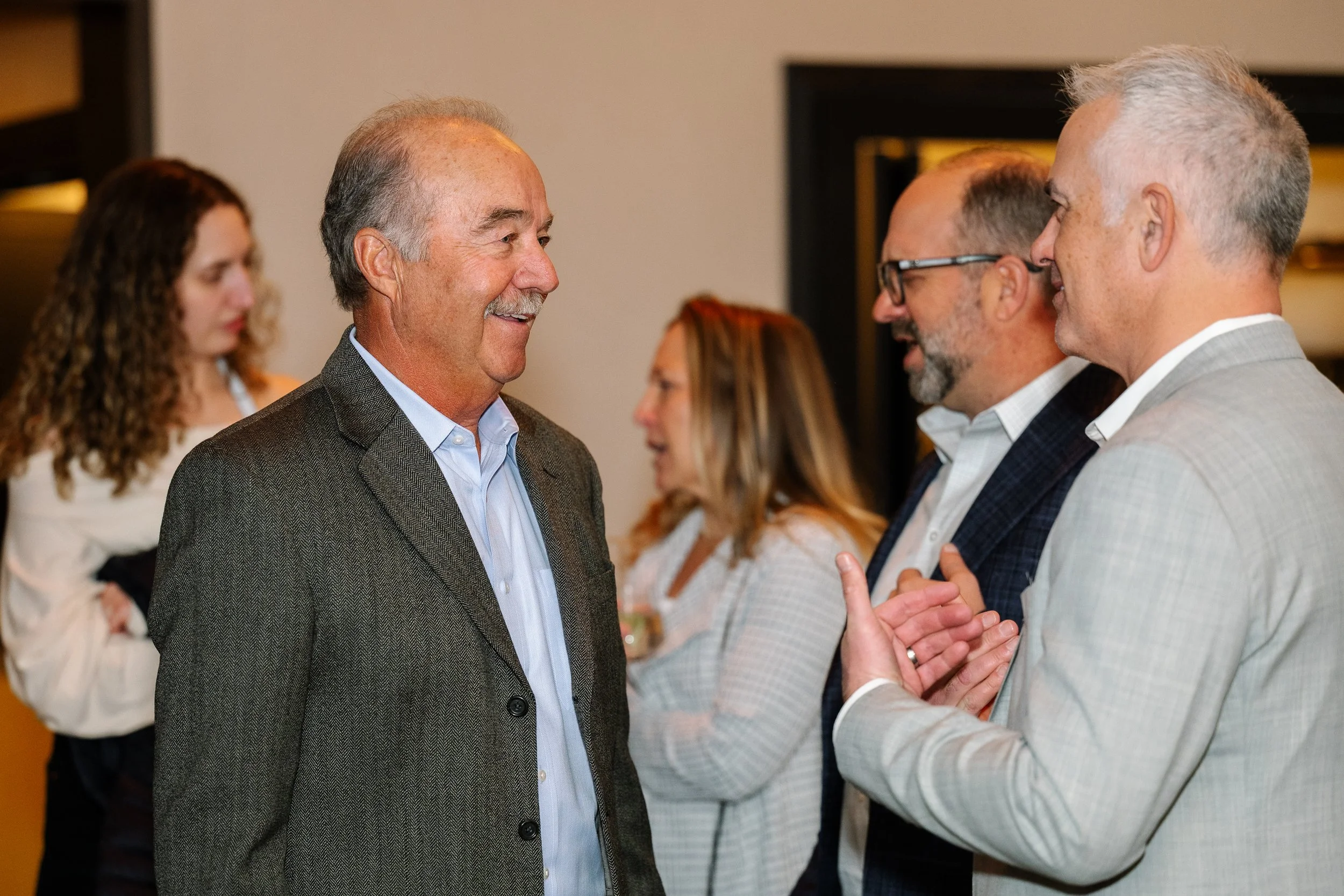 A group of professionally dressed people engaging in conversation at a social or networking event in an indoor setting.