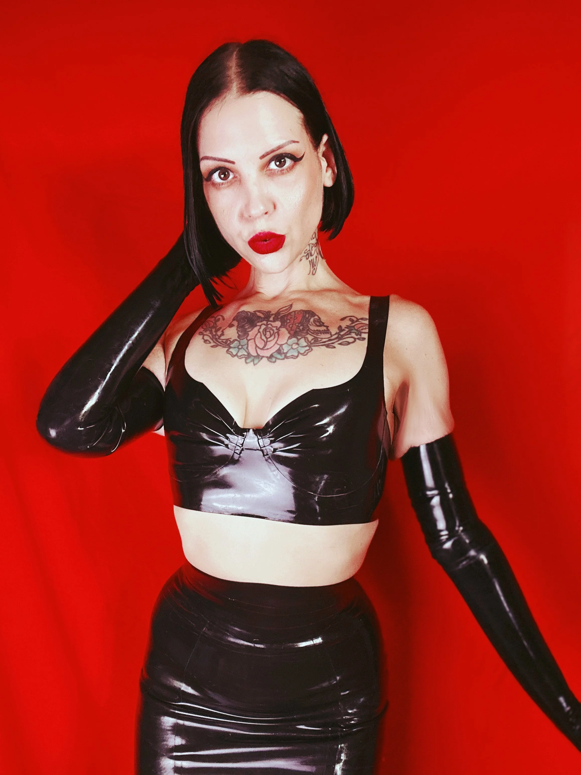 Chicago femdom Mistress Maddie Royce, a portrait in black latex on red.