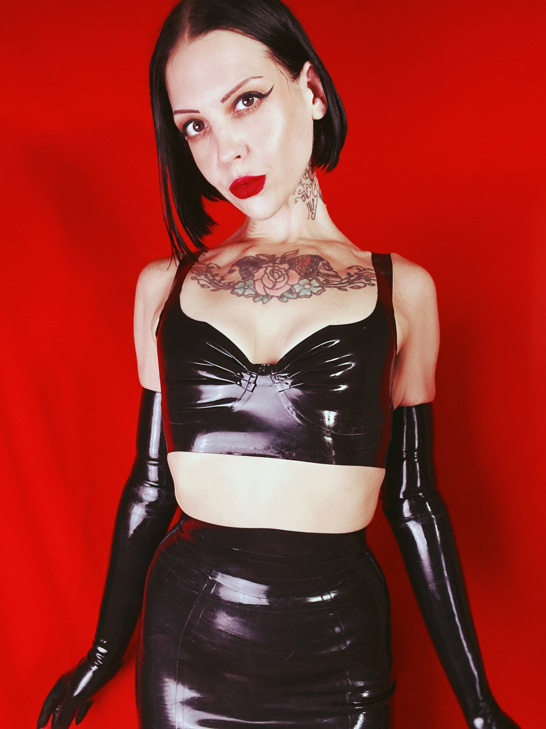 Mistress Maddie Royce, a Chicago BDSM dominatrix, in black latex against a red backdrop.