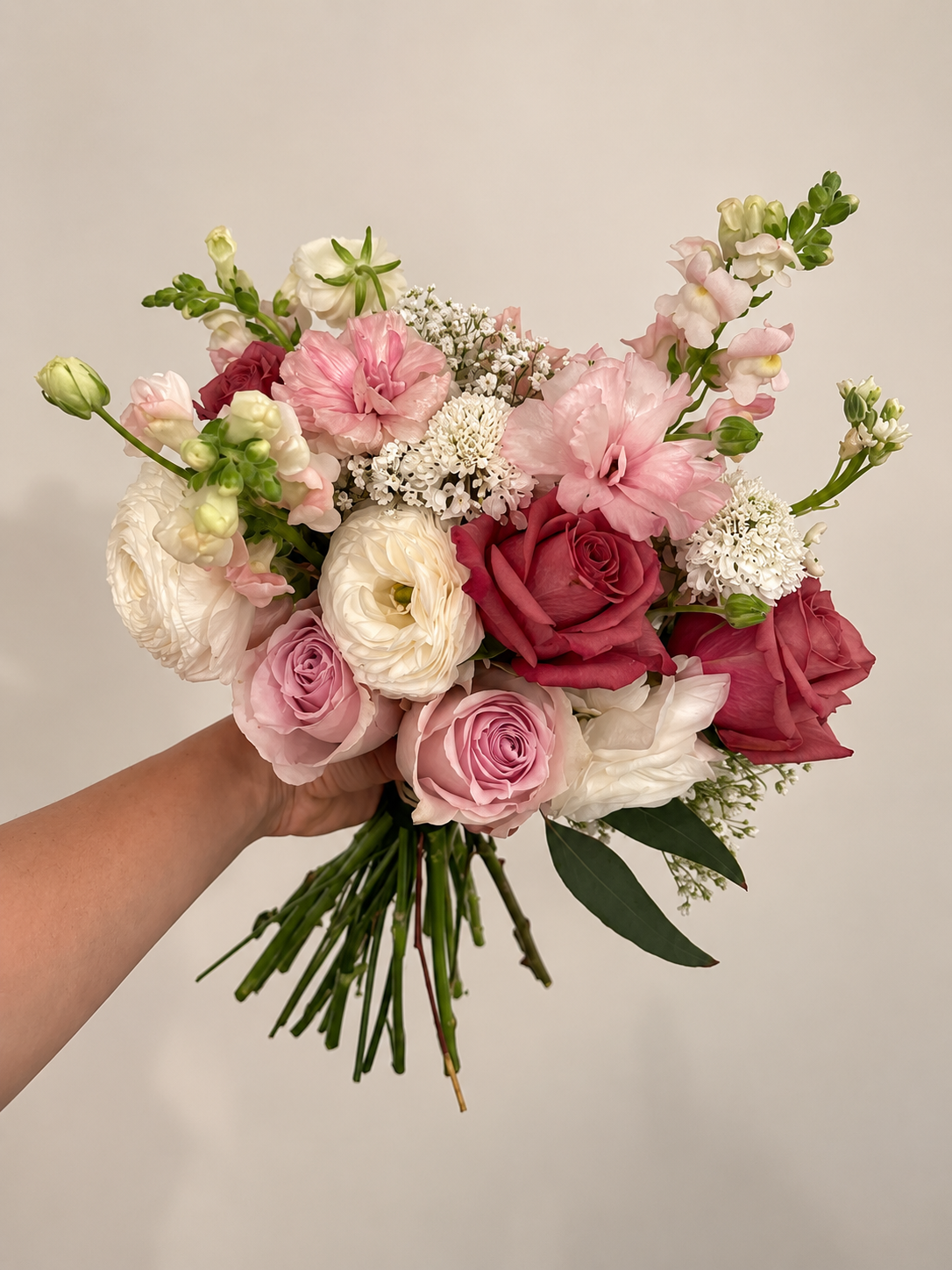 Bouquet de fleurs multicolores composé de roses, lisianthus, et autres fleurs, tenu par une main
