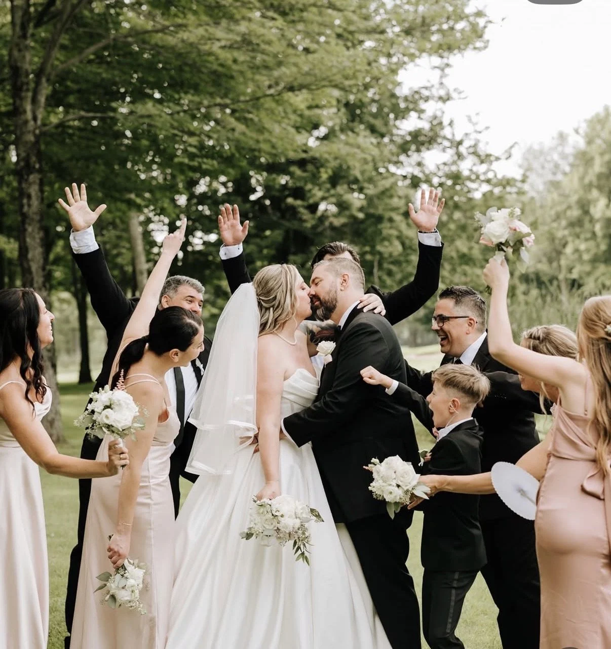 Un couple de mariés s'embrassent entourés de leurs amis lors d'un mariage en plein air dans un parc.