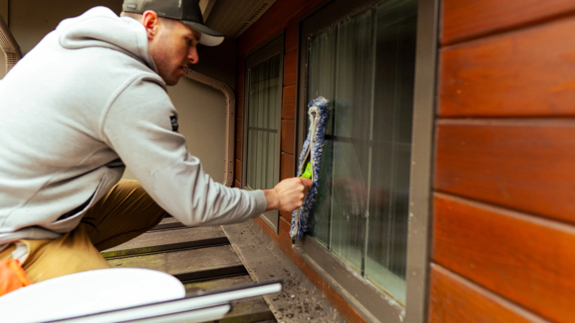 A man cleaning a window with a cloth outside a building, wearing a gray hoodie and a cap. - Taken by Dillon Morby of D Morby Media, a local photographer working in South East Michigan