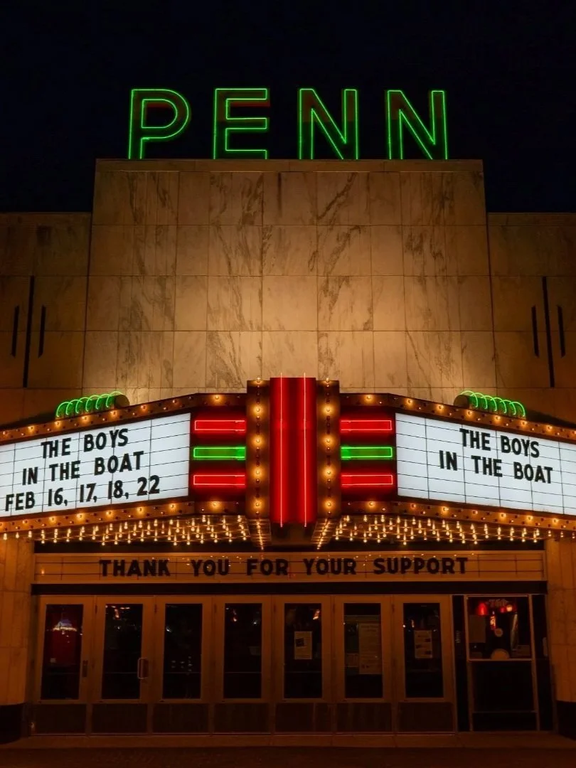The Penn Theatre at night with neon green 'PENN' sign on the roof and a marquee advertising 'The Boys in the Boat' showing on February 16, 17, 18, and 22, with a gratitude message for support.