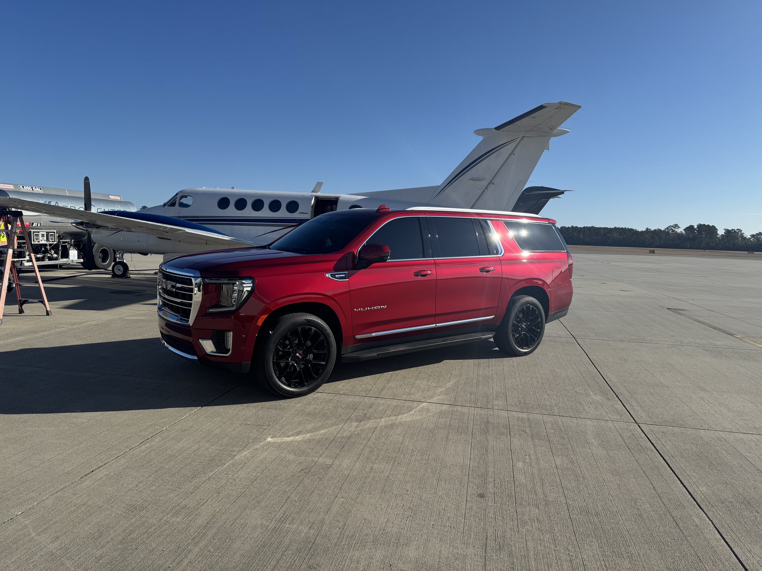 A red SUV truck parked on an airport tarmac near a private jet airplane.