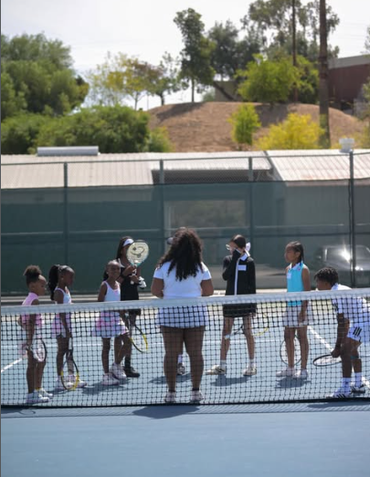 Children on a tennis court receiving instruction from a coach during a soccer practice or camp.