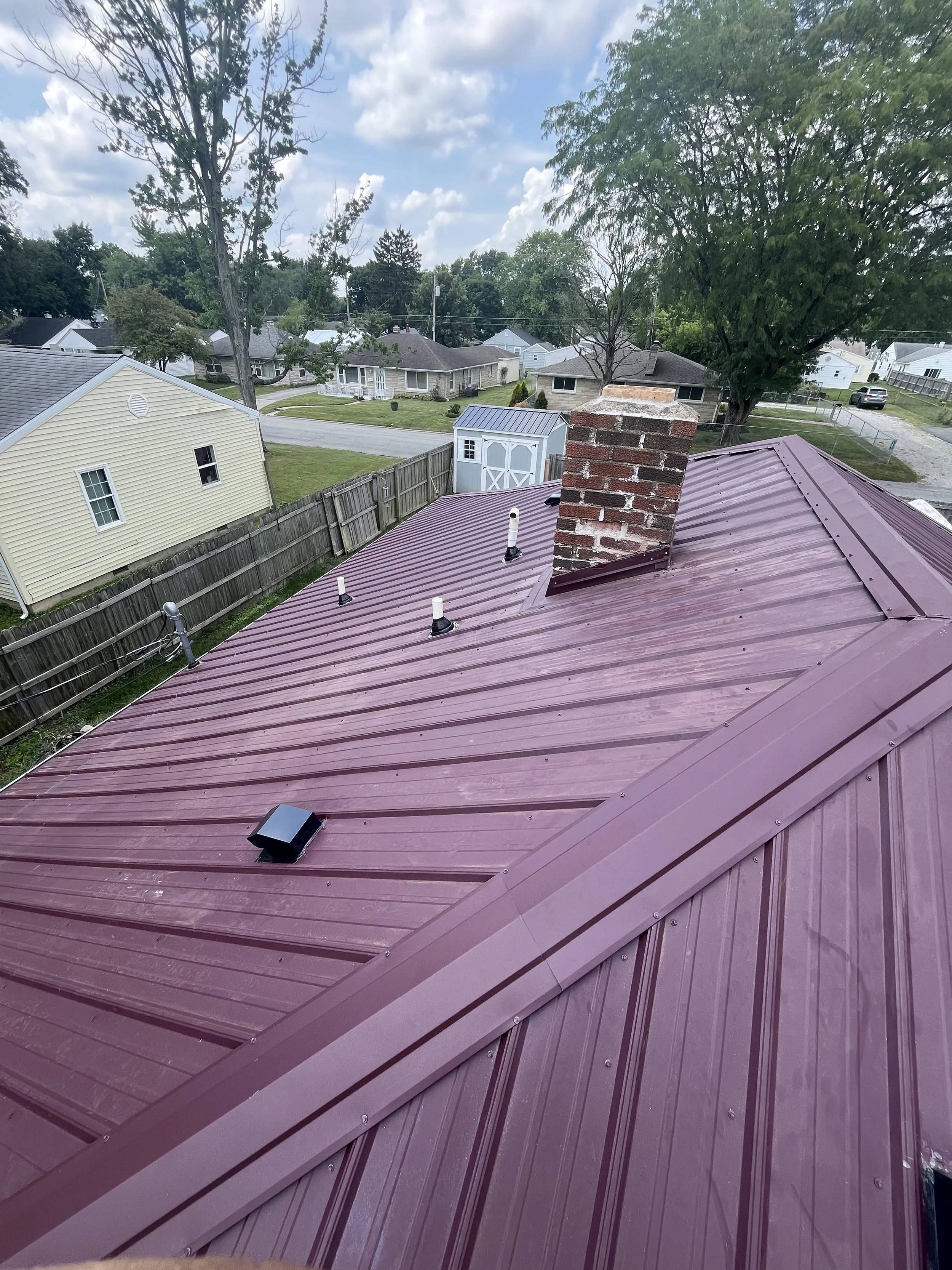 View from a rooftop showing neighboring houses, trees, and a partly cloudy sky.