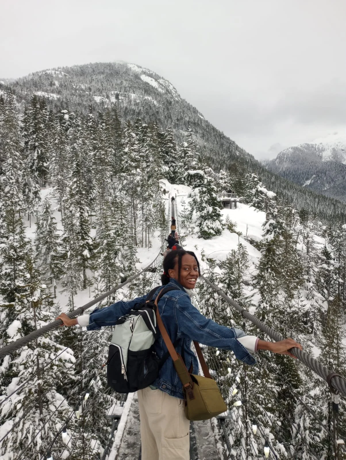 Victoria smiling on a suspension bridge in a snowy mountain forest during winter.
