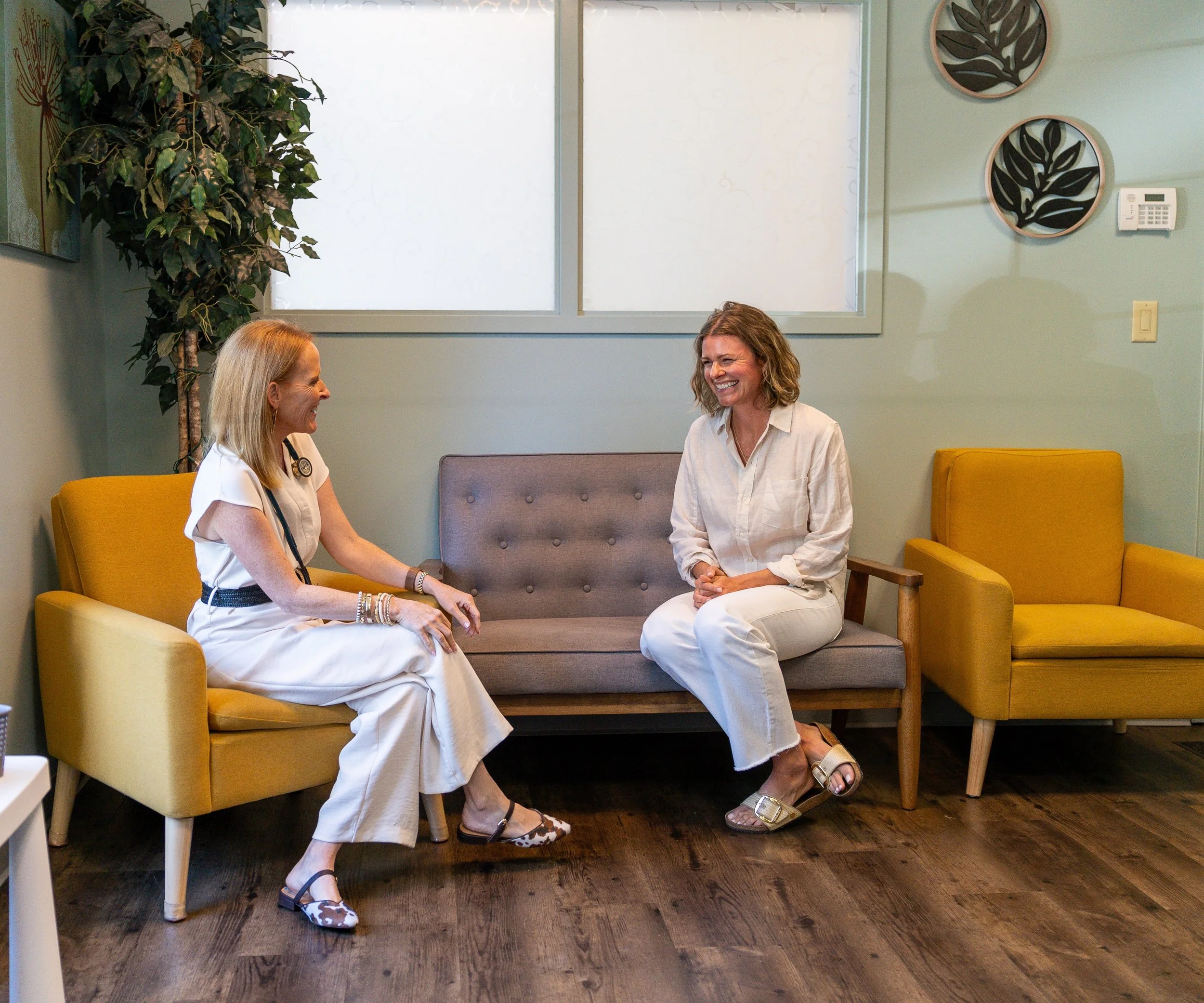 Two women talk and laugh with each other as they sit on comfy chairs