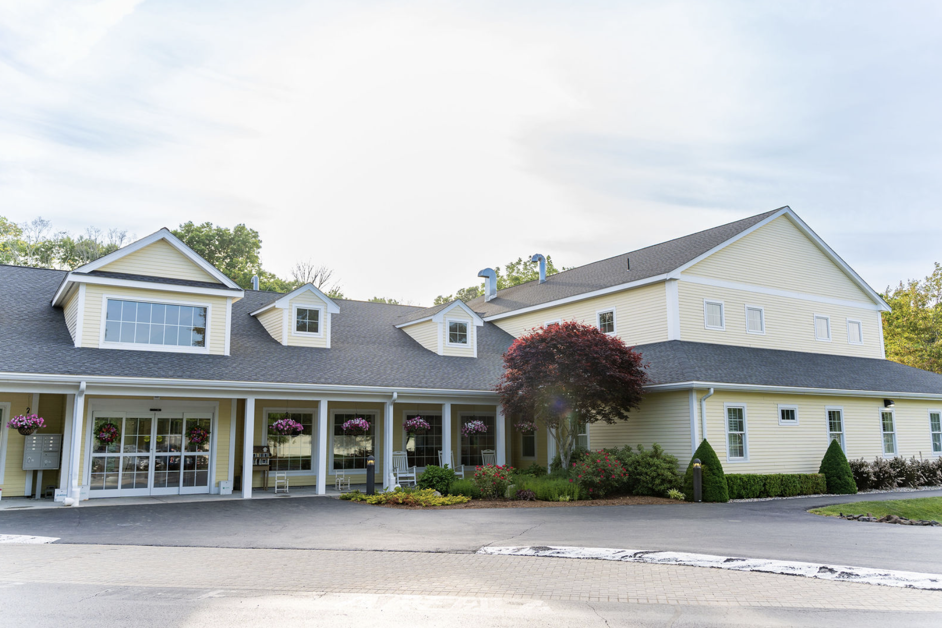 Exterior image of a yellow building with shrubs, plants, and flowers surrounding it.