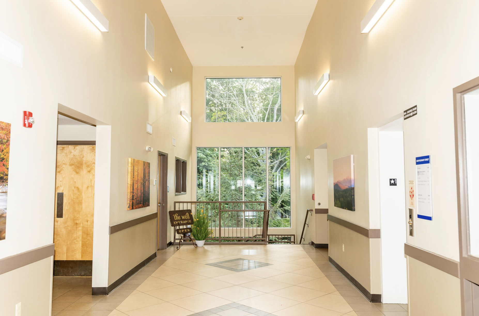 An interior space with high ceilings, large windows, and an open stairwell. To the left there is a sign that reads "The Well Entrance"