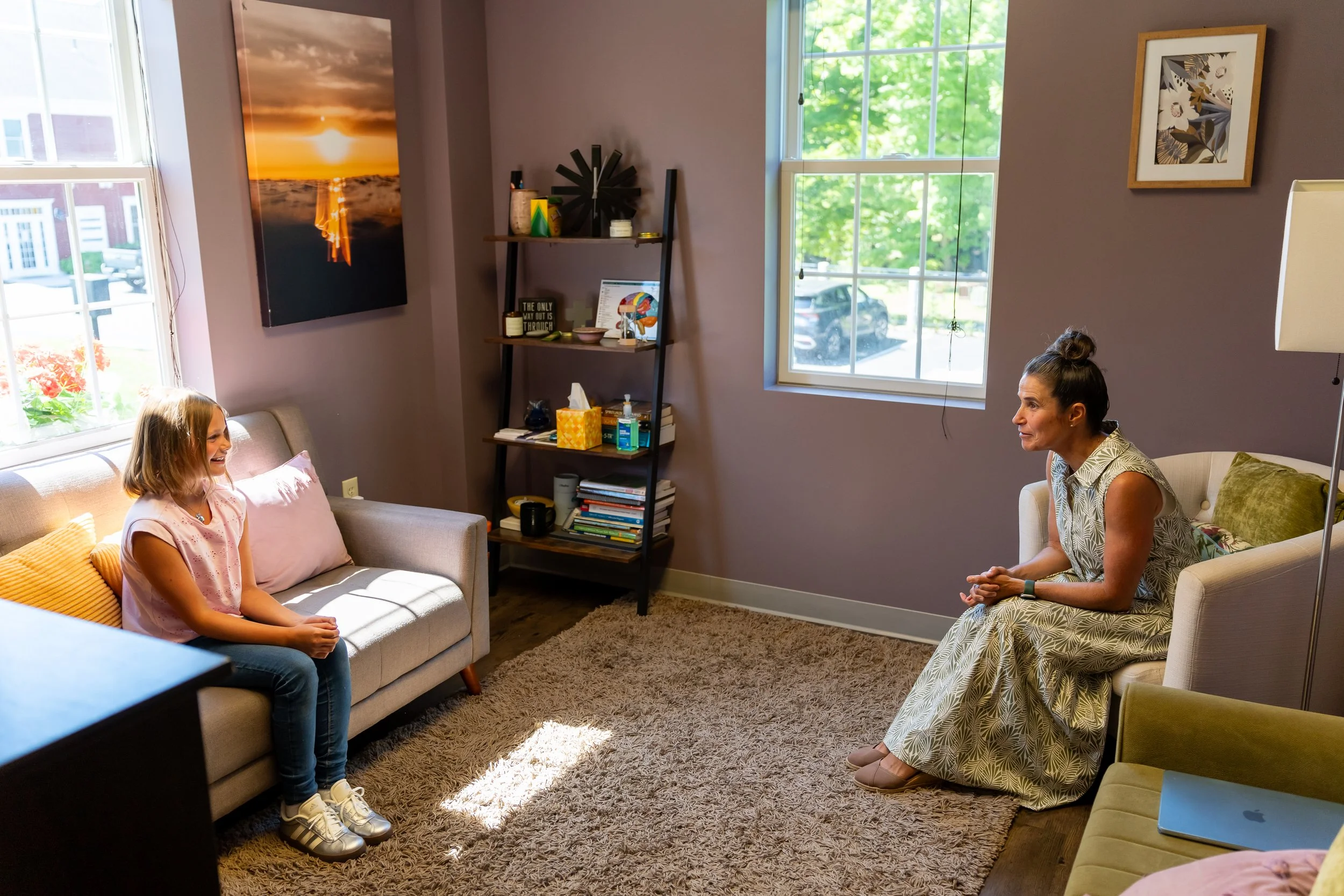 A therapist sits across from a young girls as they smile and talk to each other.