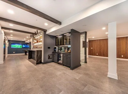 Modern basement with bar, dark cabinetry, and open space with wood paneling on walls