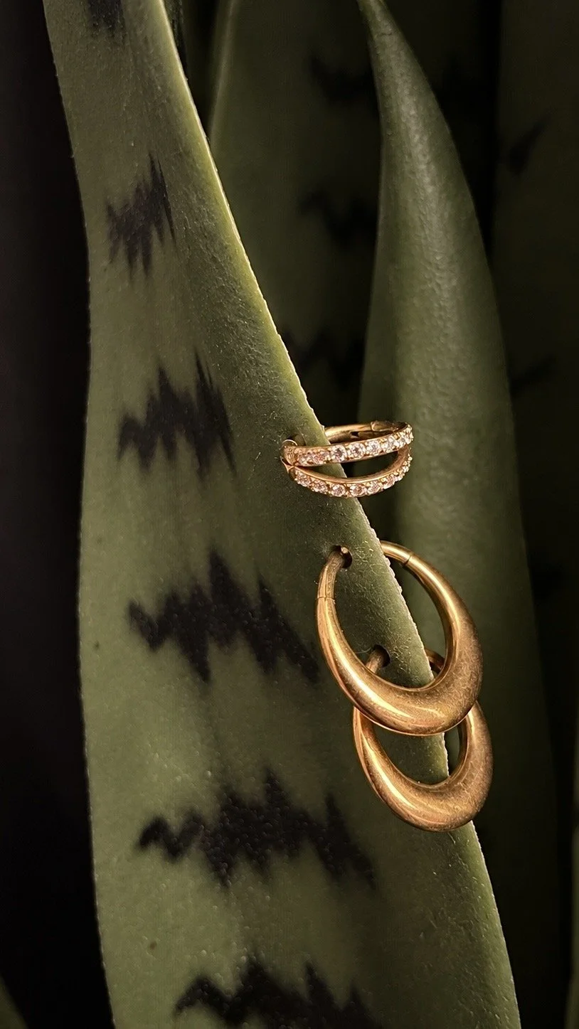 Gold earrings resting on green plant leaves with black spots.