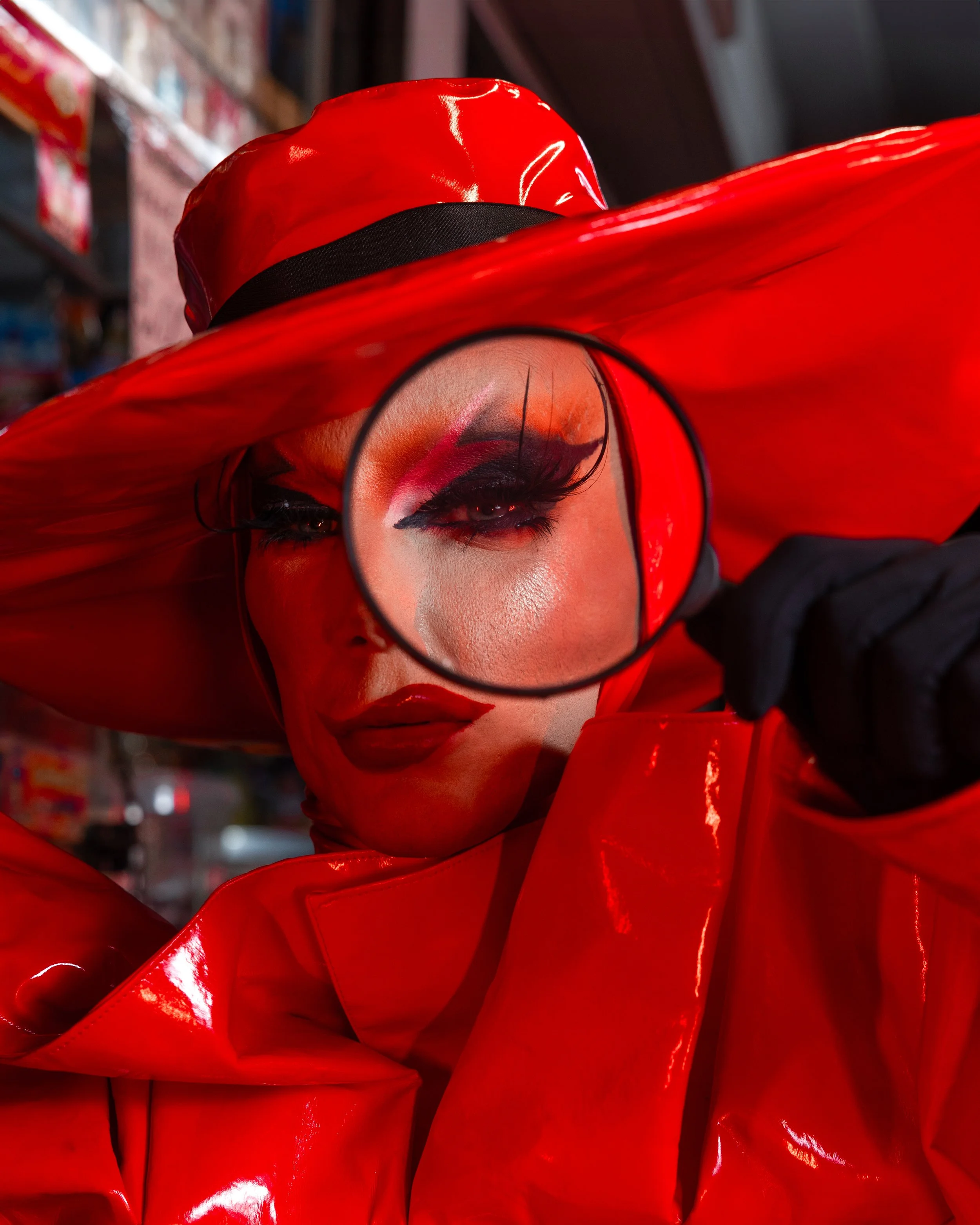Pessoa com maquiagem dramática e roupa vermelha brilhante, usando um chapéu ou acessório vermelho, visual artístico e ousado, segurando ou usando um espelho.
