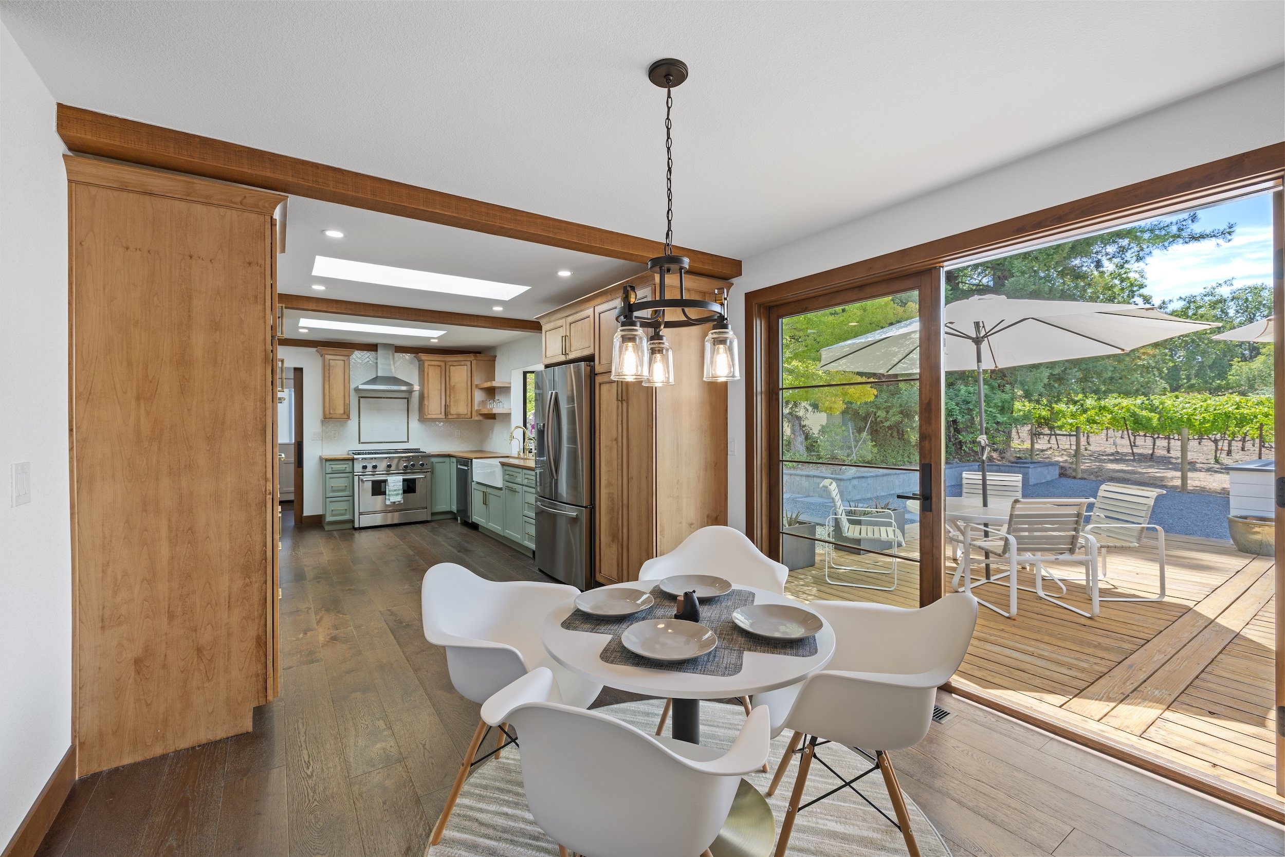 Interior view of a modern kitchen and dining area with large sliding glass doors leading to a patio with outdoor furniture and a vineyard in the background.