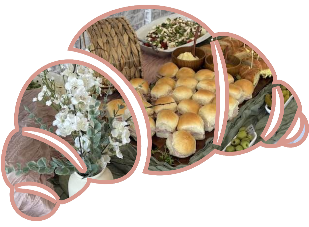 A table with a vase of white flowers and a spread of bread rolls, salad, and appetizers.