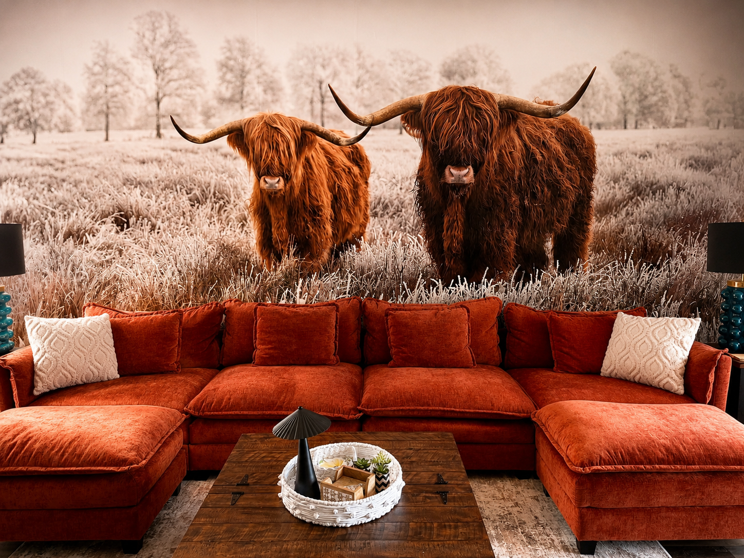 Highland cattle mural accent wall in a cozy living room with a red sectional sofa, wood coffee table, and warm lighting.
