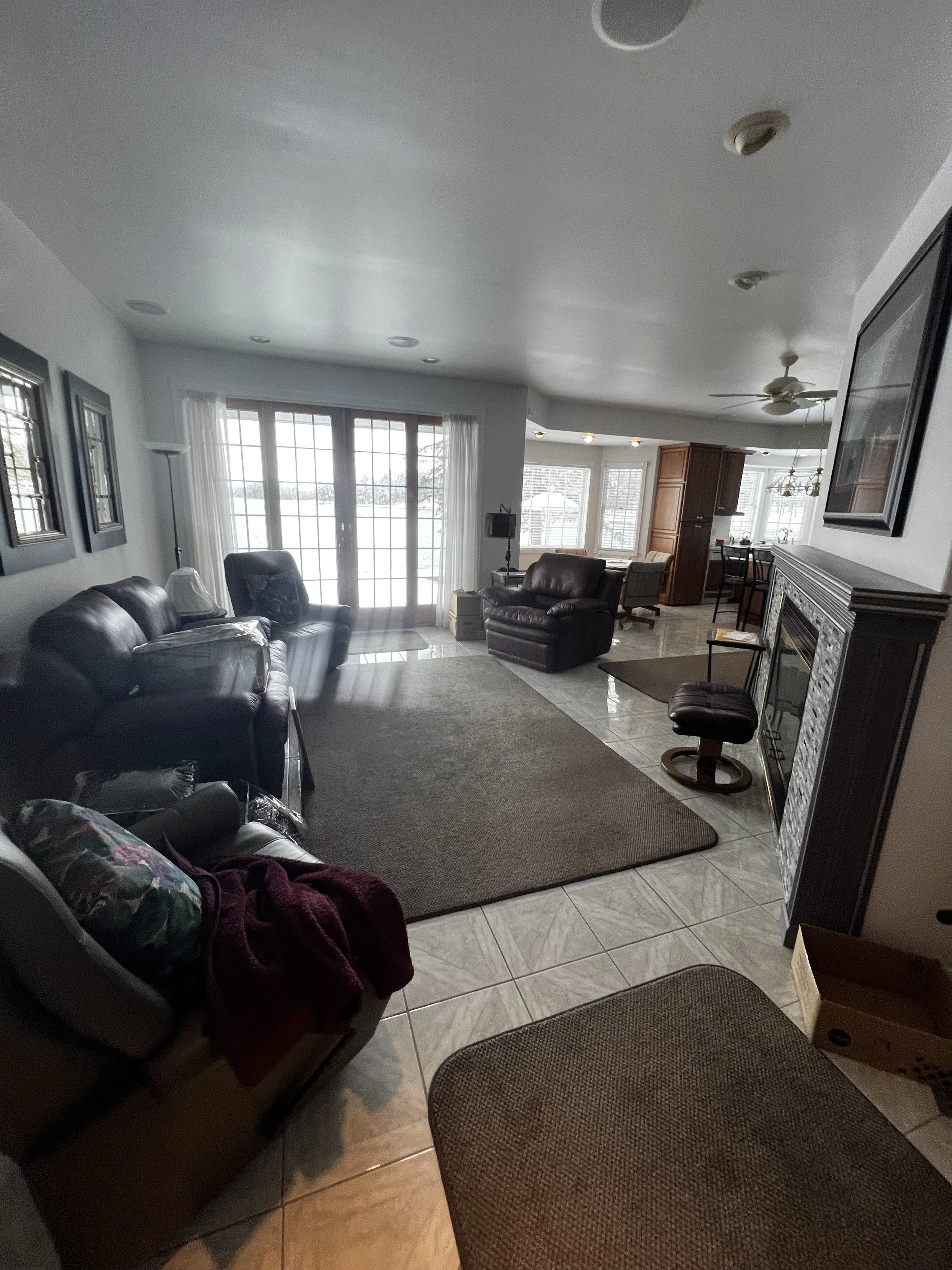 Living room with leather couches, a patterned rug, large windows with white curtains, a fireplace, and various chairs and tables.