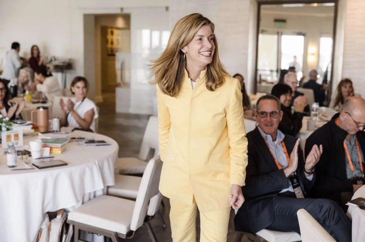 Dr. Kerry Burnight smiling as she walks onto a stage in a yellow suit