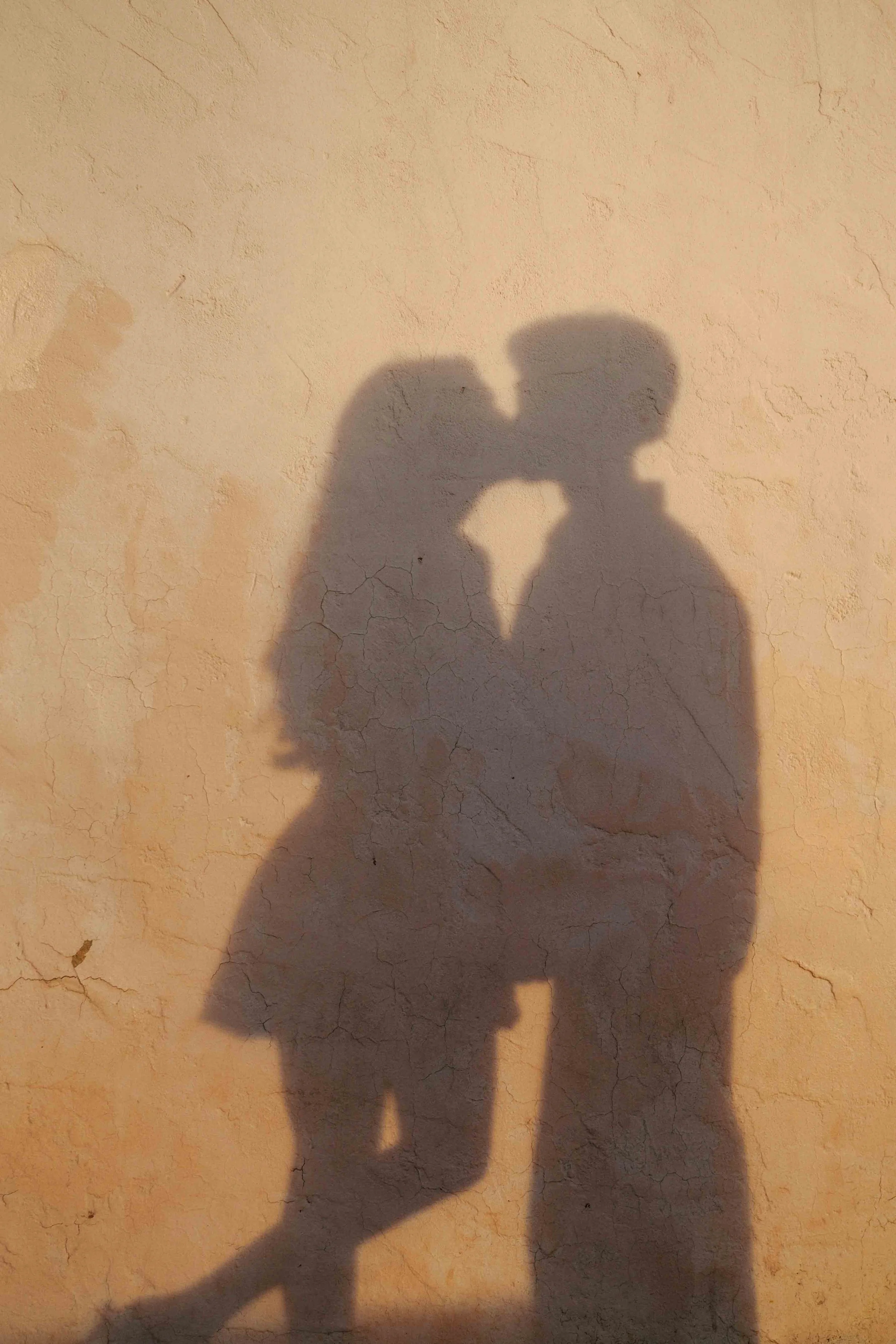 Shadow of a couple kissing on a textured beige wall.
