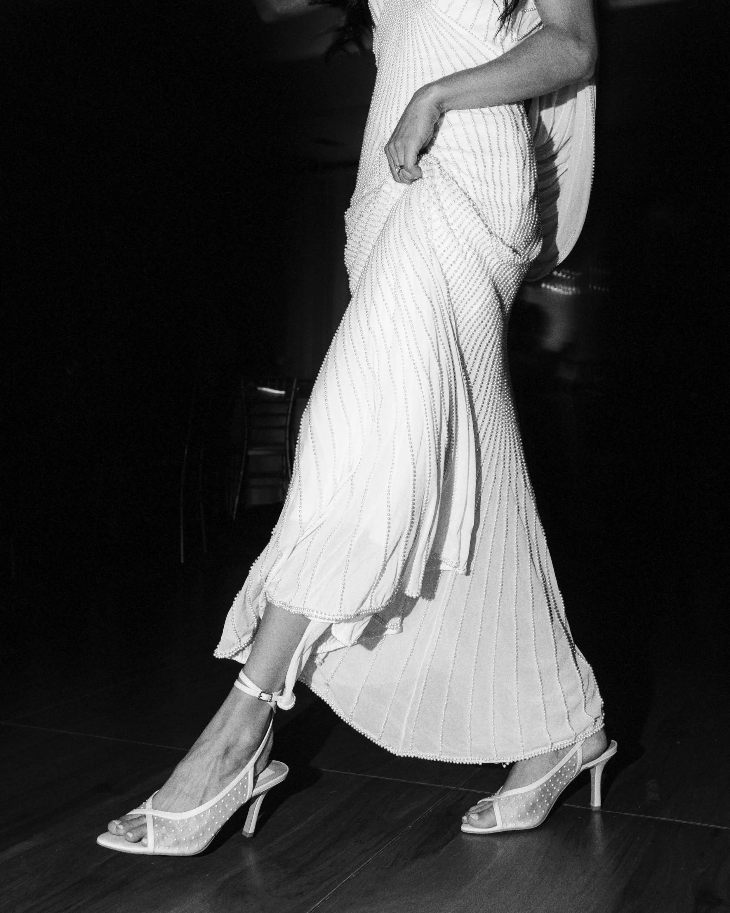 Close-up of a woman wearing a beaded dress and high heels, showing her legs and part of her dress, in black and white.