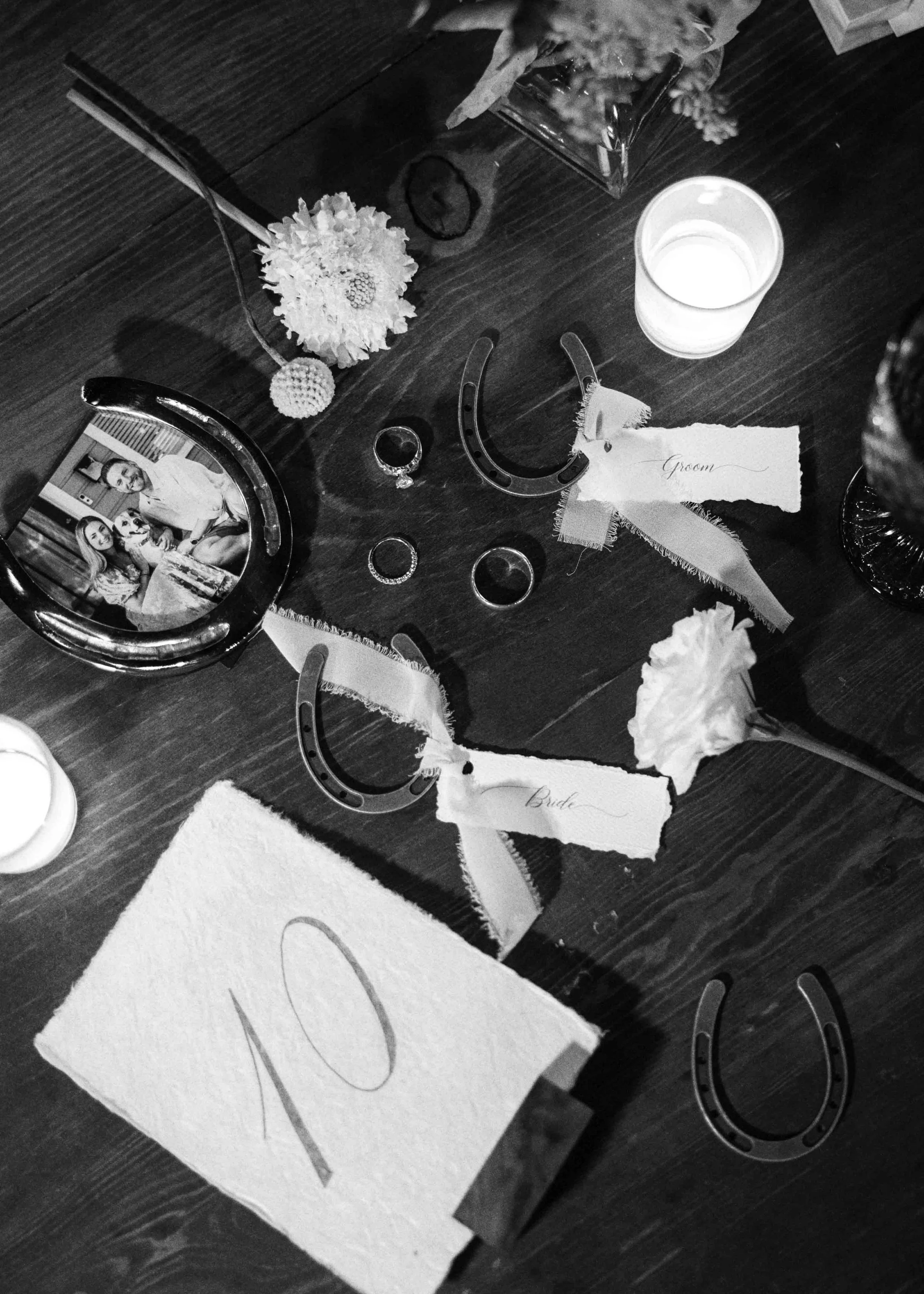 A table decorated for a wedding with flowers, a photo frame, wedding rings, and a 'Groom' and 'Bride' name tags.