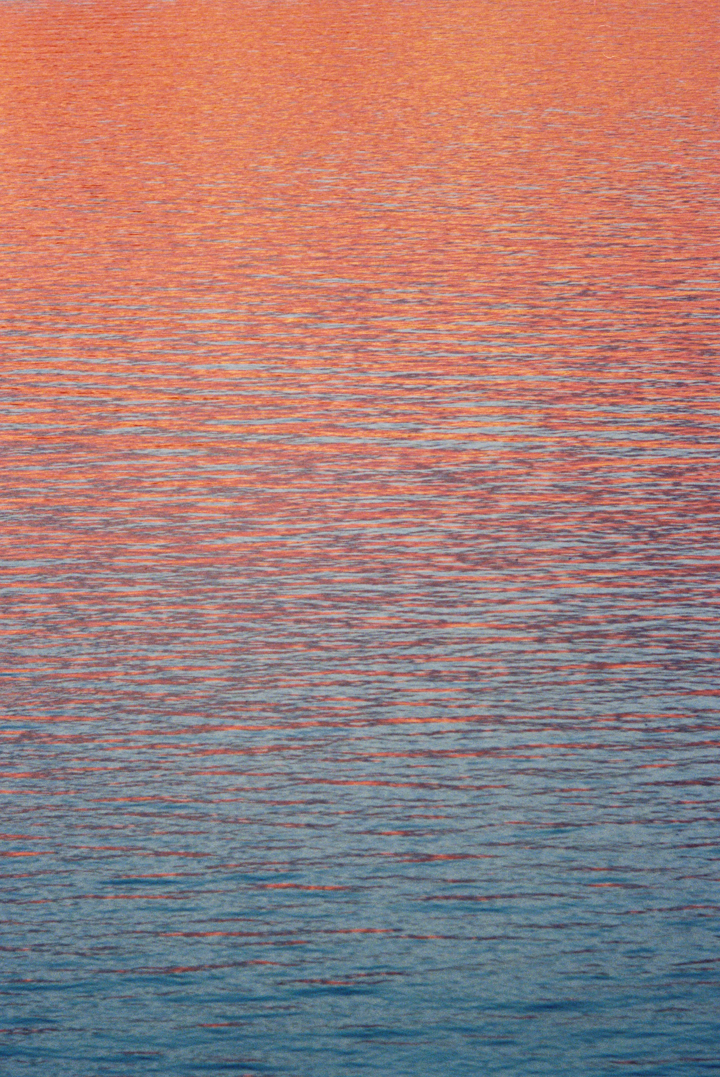 A body of water at sunset with pink, orange, and purple hues reflecting off the surface.