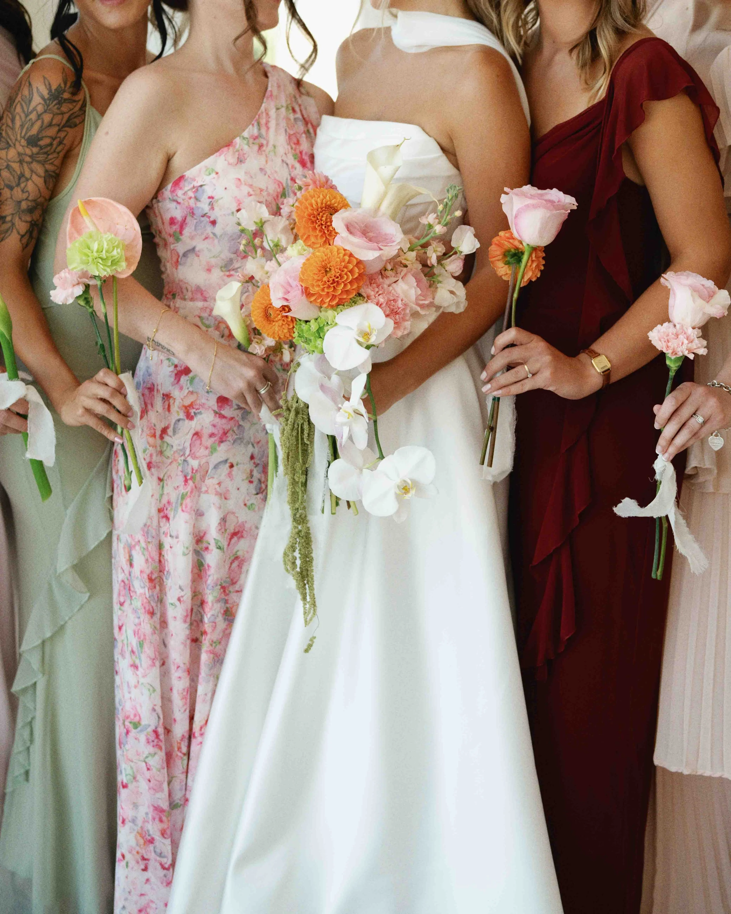 People at a celebration, holding bouquets of flowers, including roses, calla lilies, and marigolds, dressed in colorful and elegant attire, with a focus on their upper bodies and hands.
