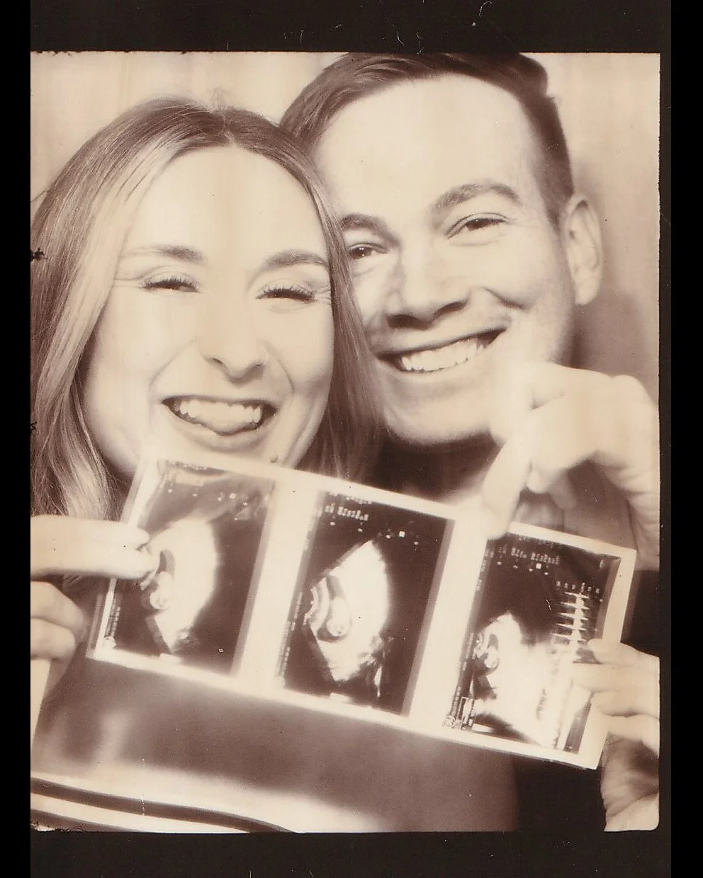 A black and white photo of a smiling couple holding ultrasound images, with the woman on the left and the man on the right.