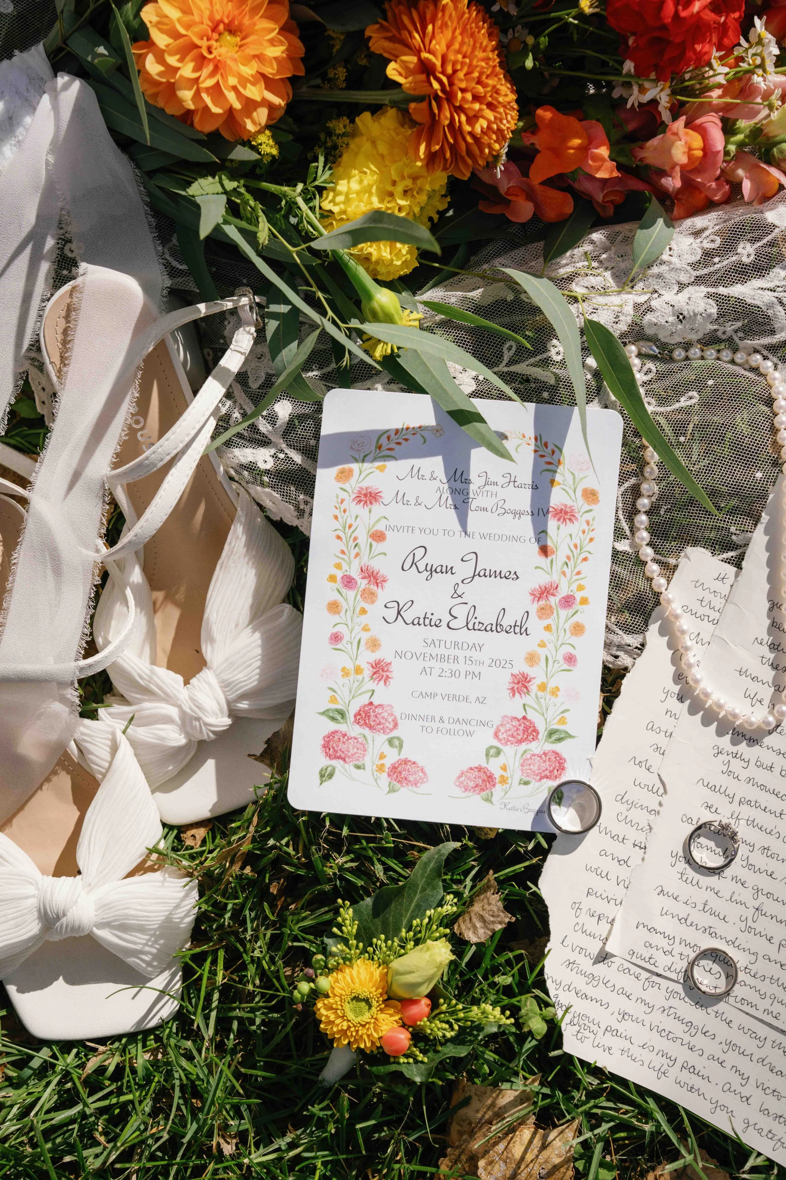 A floral arrangement including orange, yellow, and pink flowers, greenery, a pearl necklace, a pair of white sandals, a wedding invitation card, handwritten letters, and wedding rings placed on a lace fabric. The wedding invitation mentions a wedding
