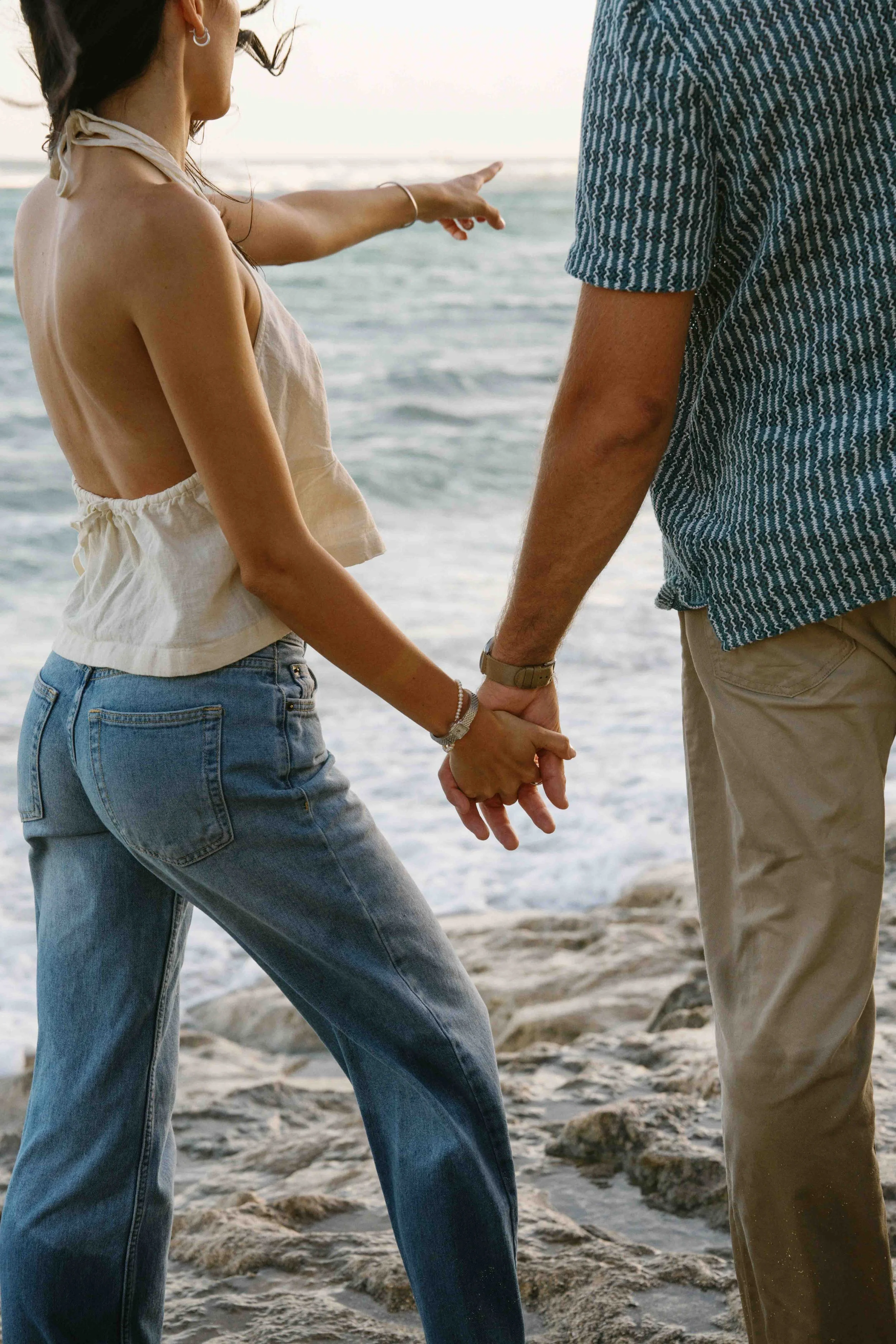 A couple holding hands at the beach while walking along the shoreline.