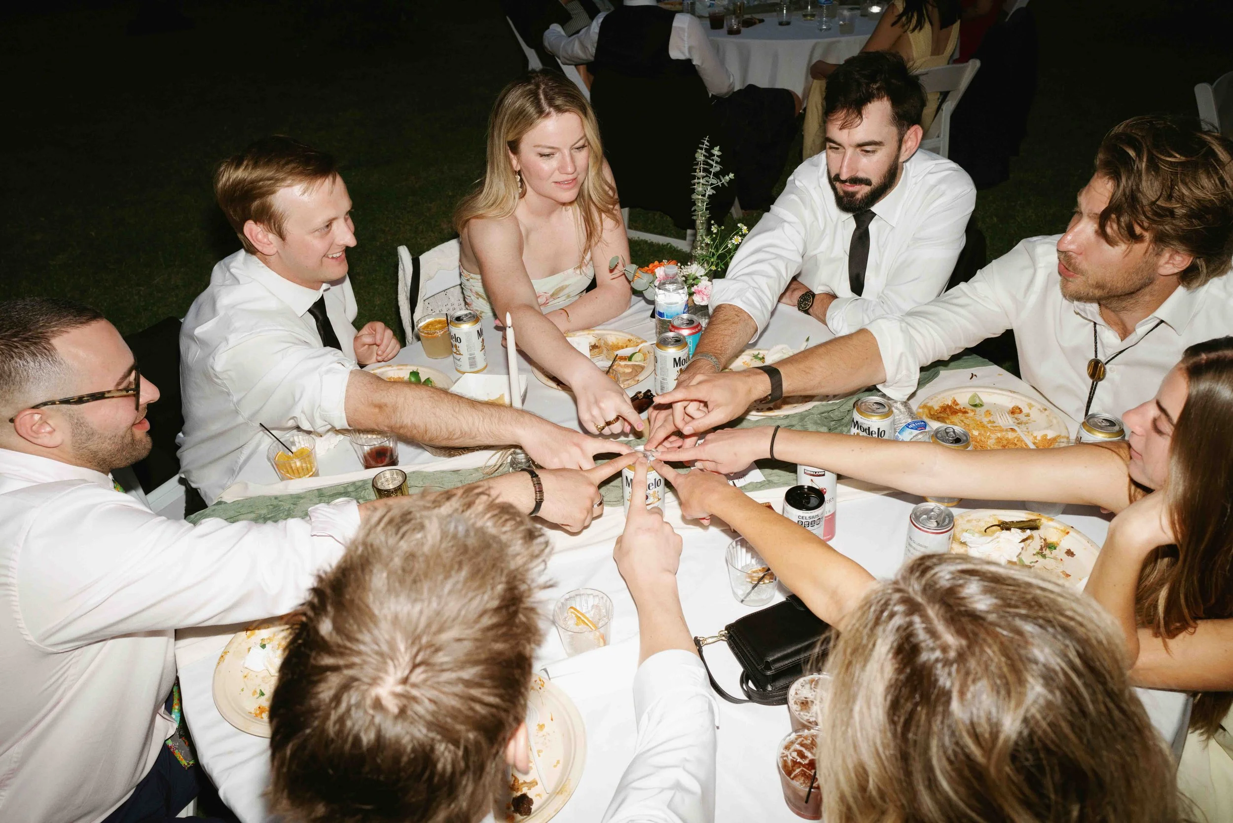 A group of people sitting around a table at night, with some passing an object to each other during a celebration or gathering.