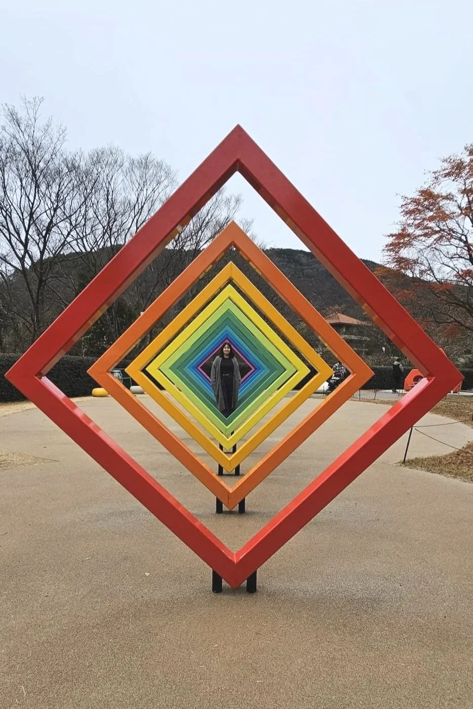 Person standing in the center of a colorful, geometric outdoor art installation with layered square frames in rainbow colors.