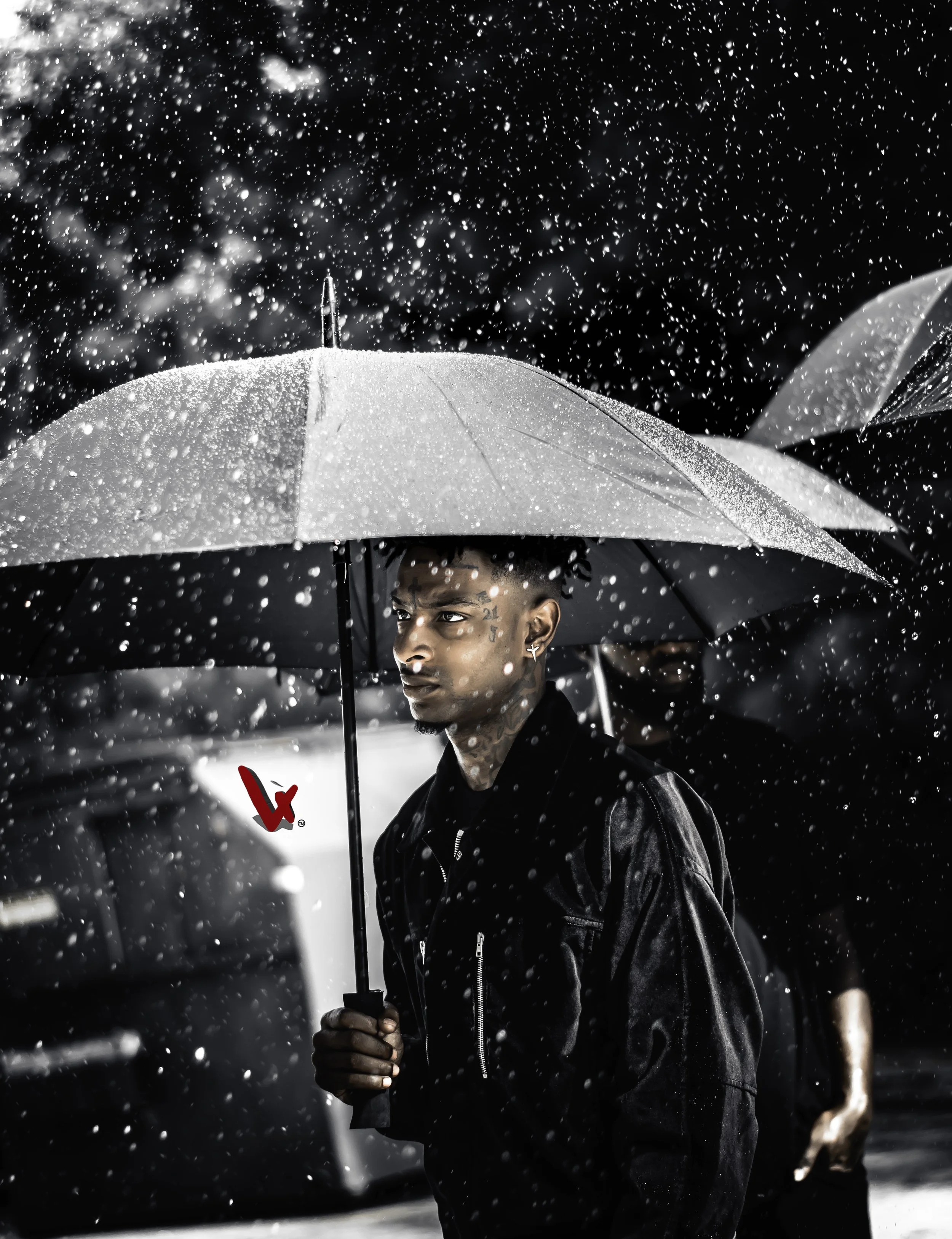 A young man with face tattoos is holding a white umbrella while standing in rain, with water droplets falling around him.