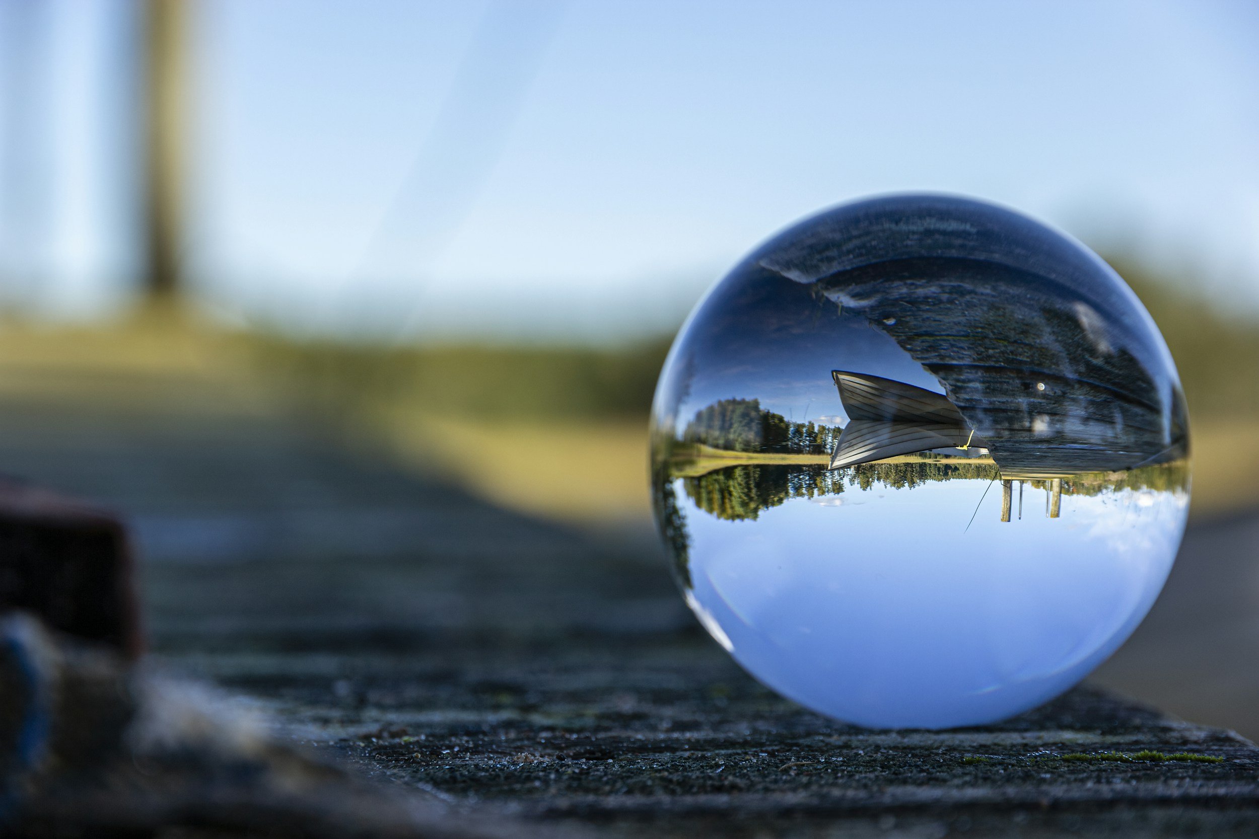 A clear glass marble reflects an image of a grassy park with trees and a blue sky, upside down.