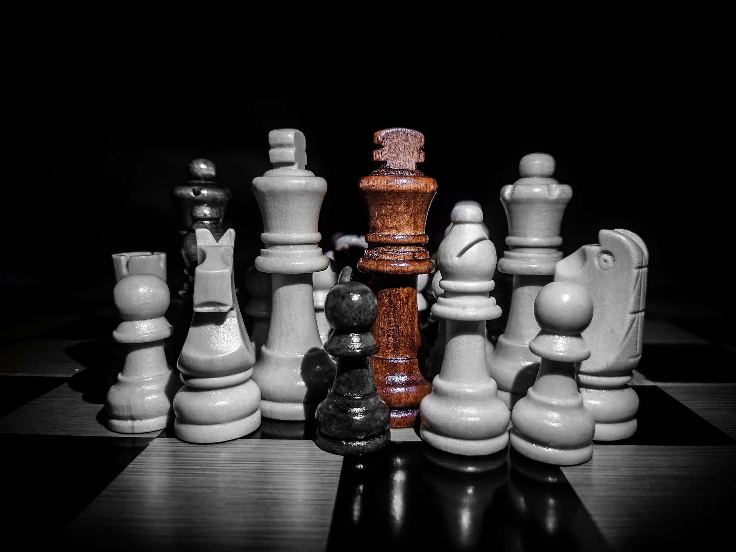 Chessboard with white and black chess pieces, featuring a central brown king, against a dark background.