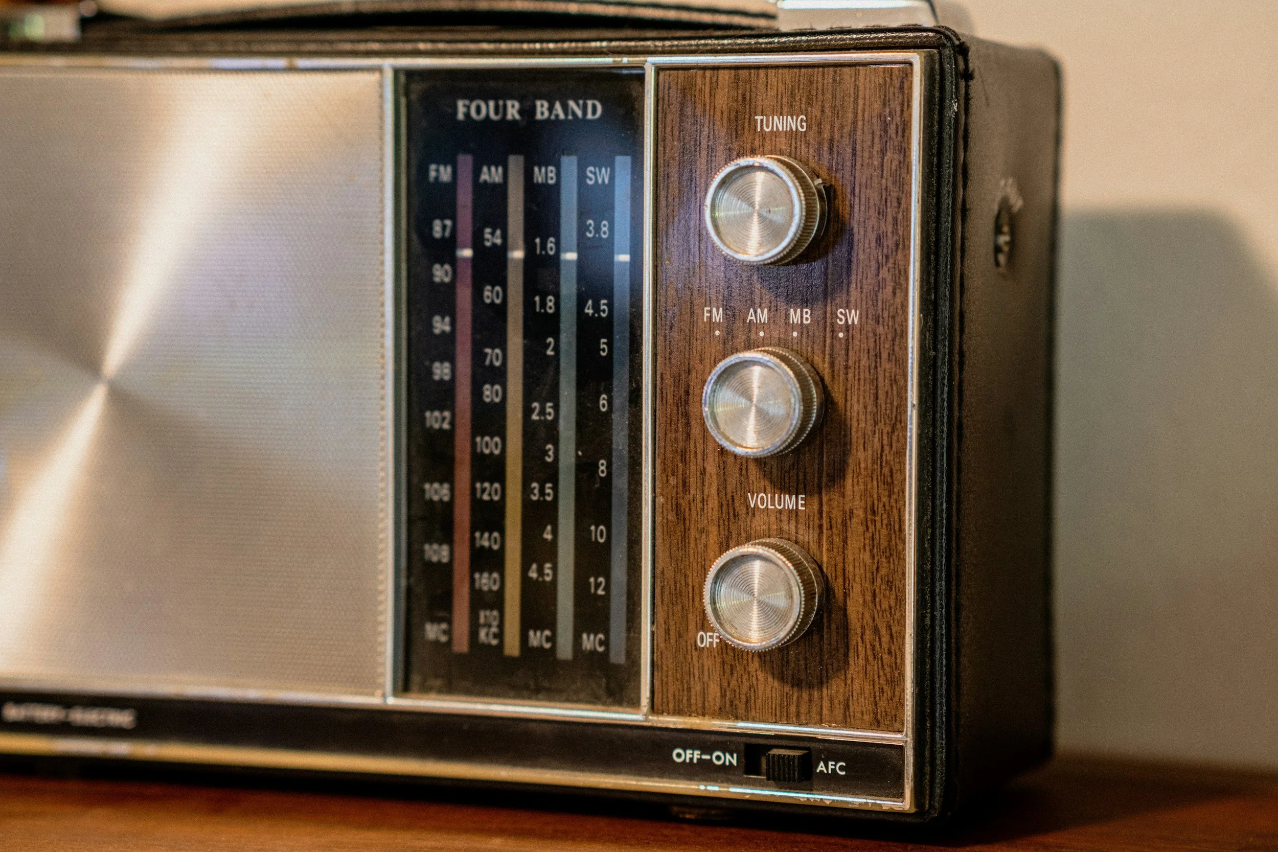 Close-up of a vintage tabletop radio with a wood finish, featuring tuning and volume knobs and a vertical frequency display.