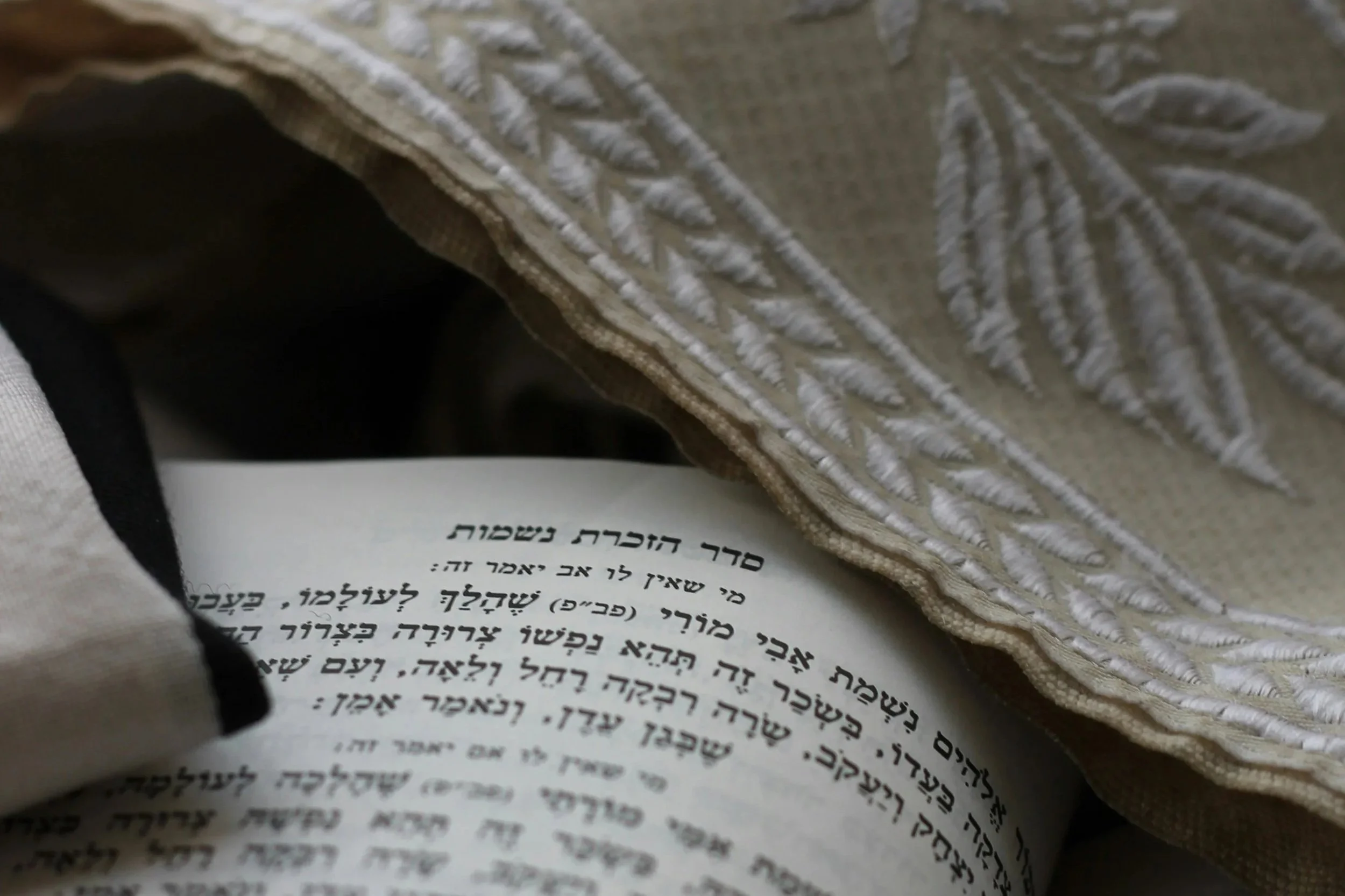 Close-up of a Jewish prayer book with Hebrew text, partially covered by a decorative fabric or prayer shawl.