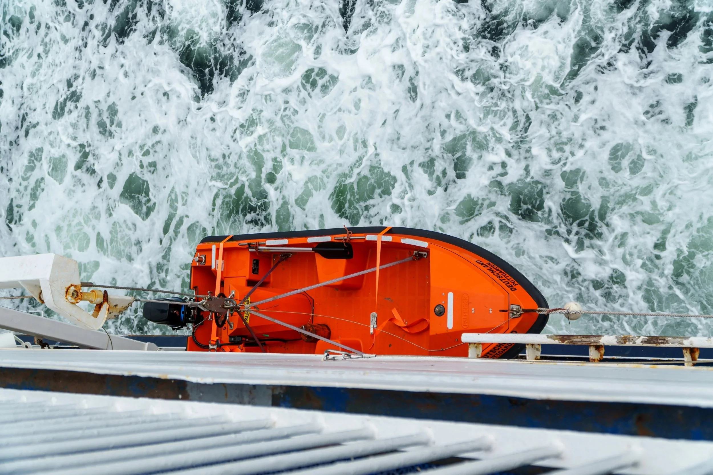 View from a boat showing orange lifeboat with safety equipment, over water with choppy waves.