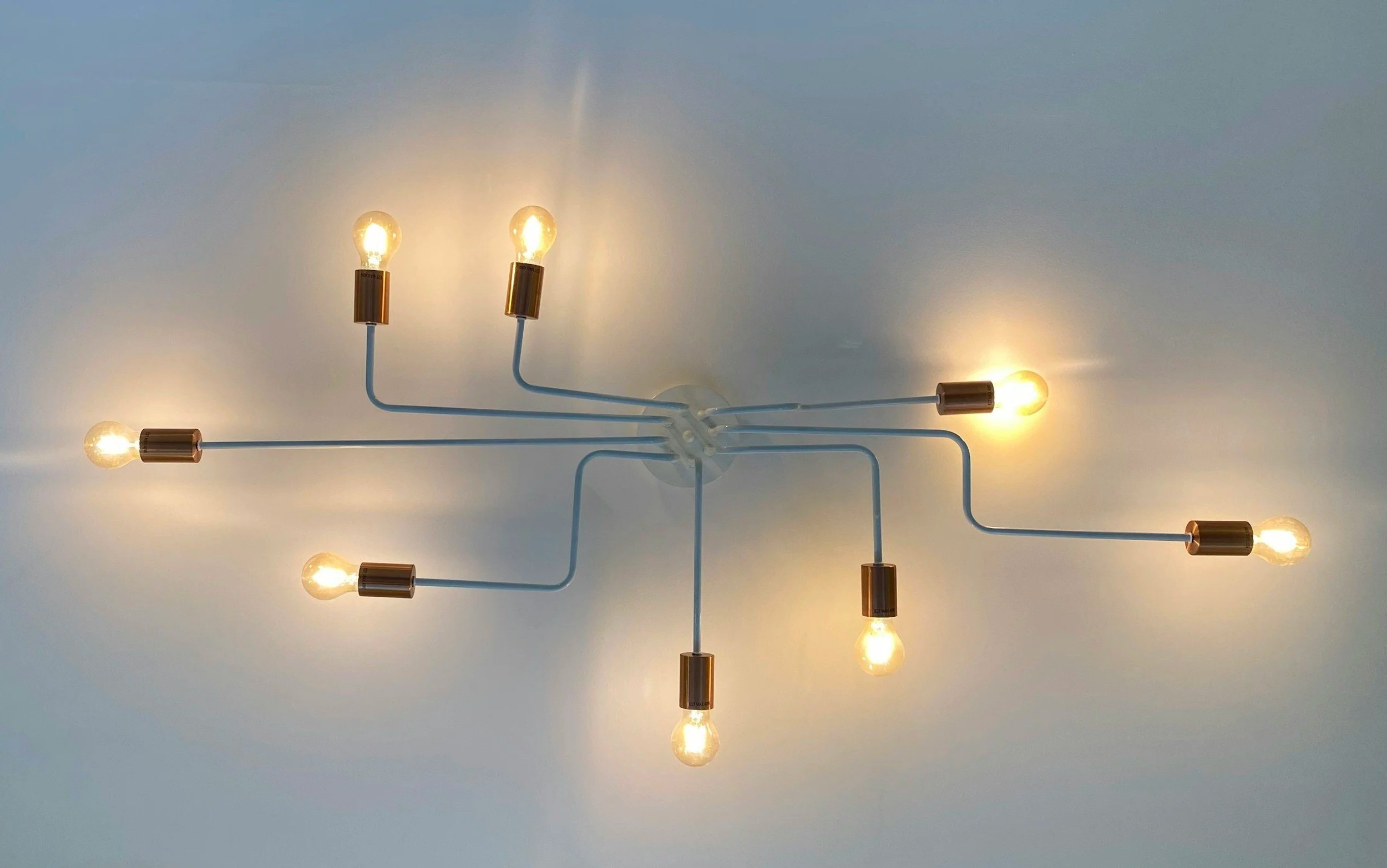 Modern ceiling light fixture with exposed filament bulbs connected by white wires with metallic gold sockets, mounted on a white ceiling.
