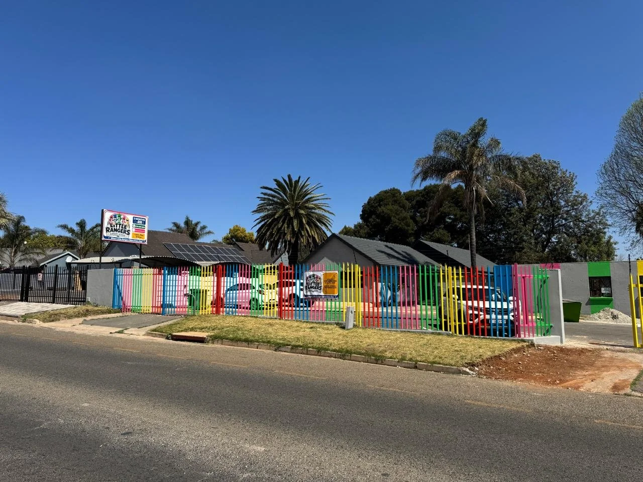 Colorful fence surrounding a building with palm trees and a bright blue sky in the background.
