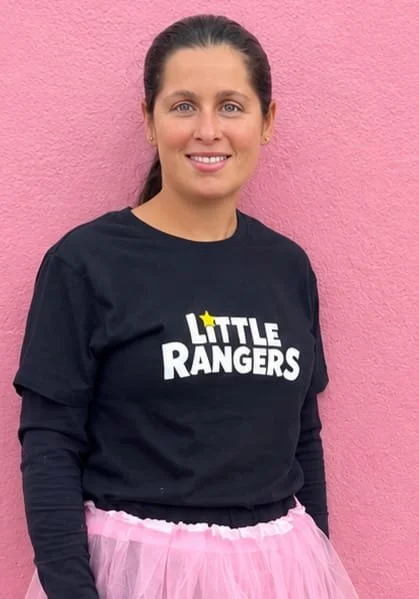 Woman wearing a black "Little Rangers" T-shirt and a pink tutu standing against a pink wall.