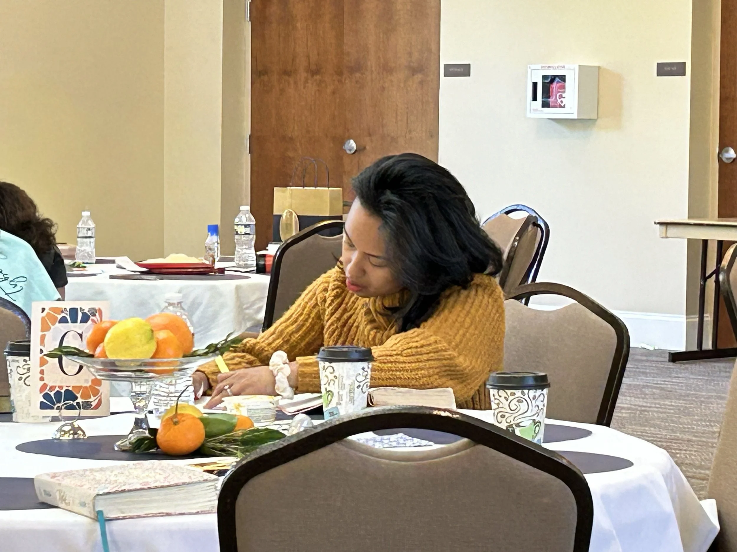 People sitting at a conference table with papers and water bottles, and a fruit bowl in the foreground
