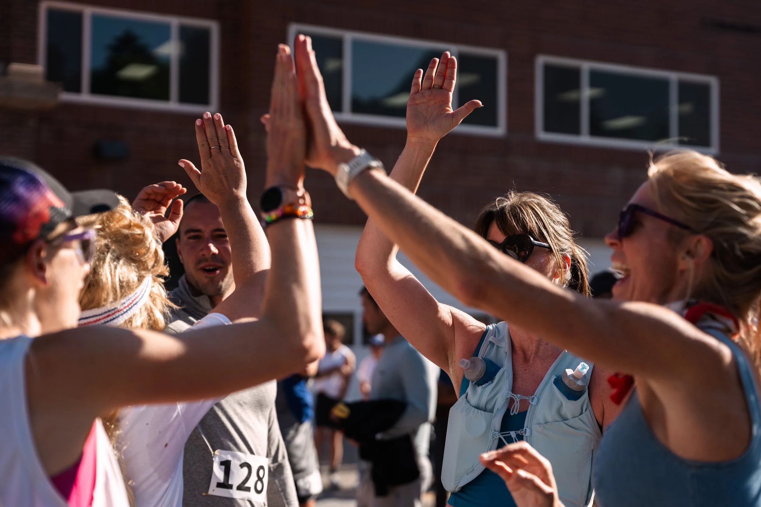 People participating in a community run or race, extending their hands for high-fives with a brick building in the background.