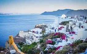Typical white buildings with pink flowers on a hillside overlooking the sea in Santorini, Greece.