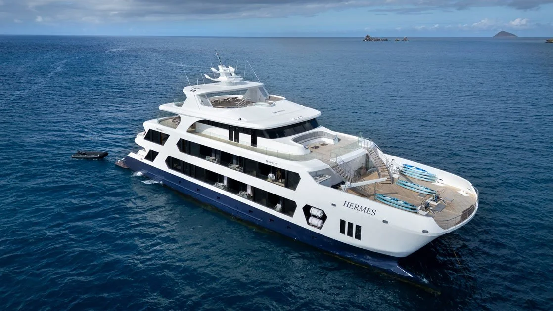 A large white luxury yacht sailing on the ocean with distant islands in the background.