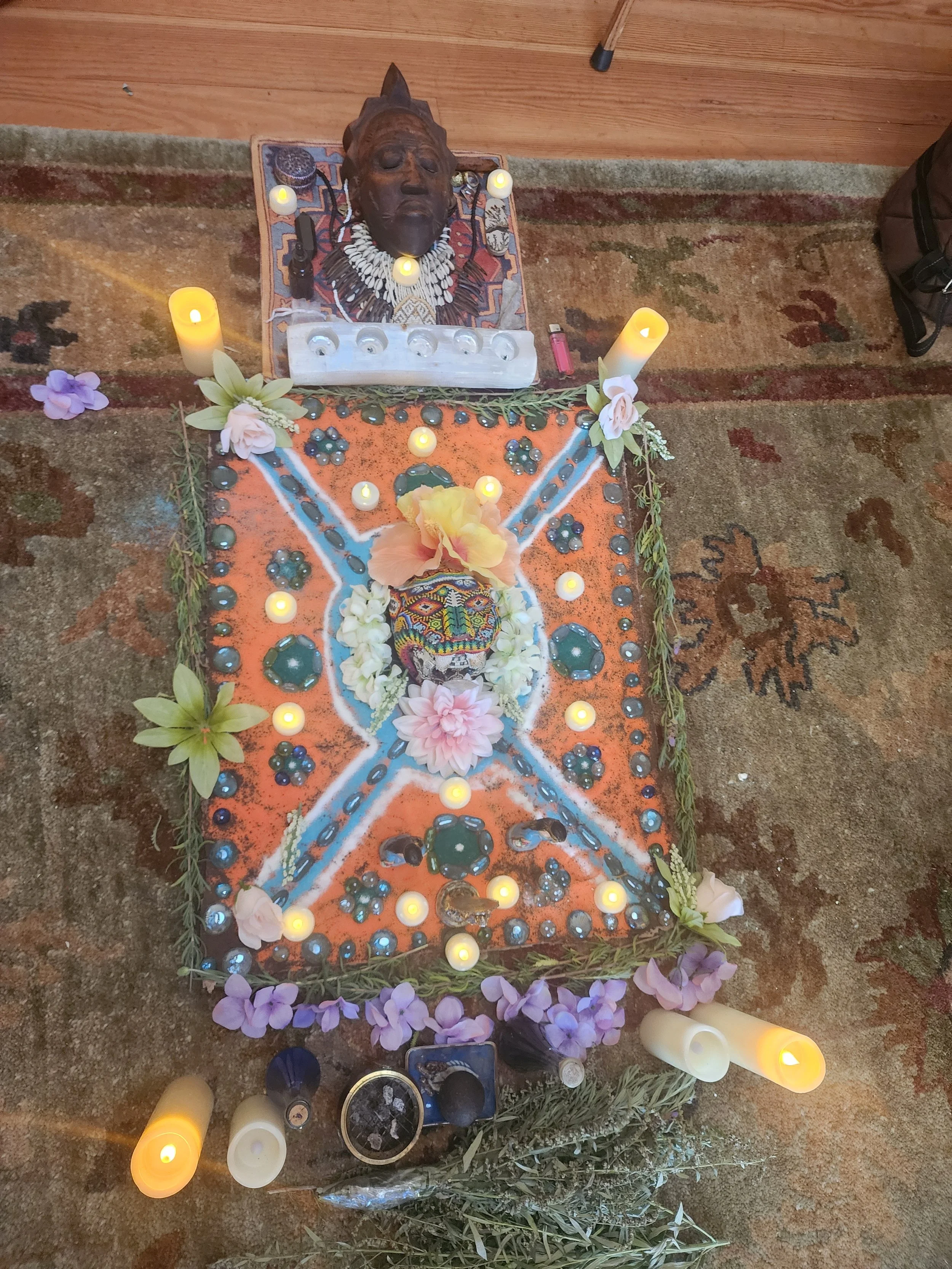 Memorial altar with a tribal mask, candles, flowers, and decorated surface for honoring someone.