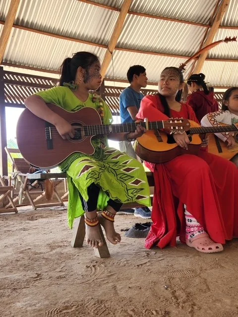 Children playing guitars inside a wooden hut