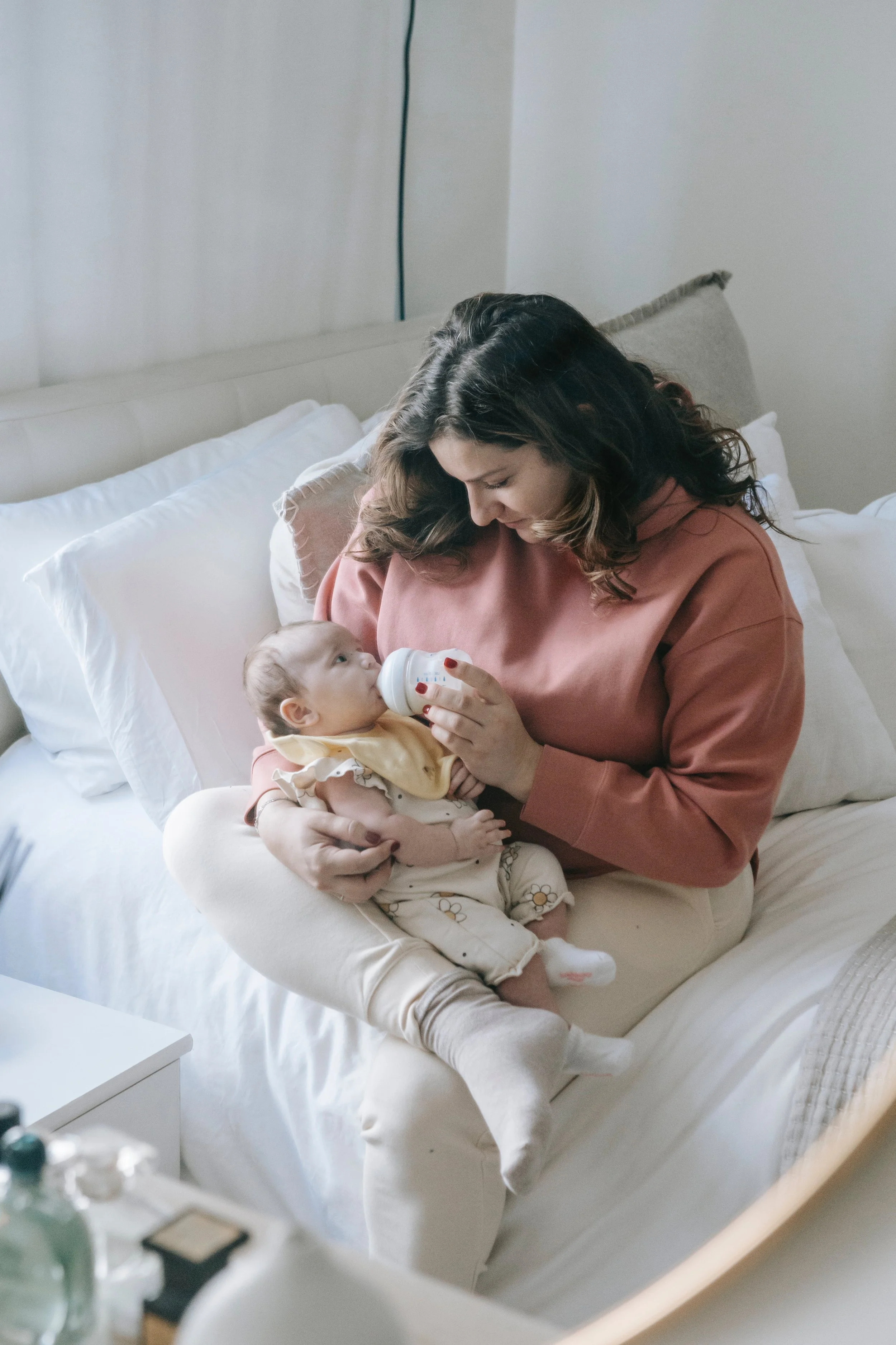 A woman feeding a baby with a bottle while sitting on a bed in a bedroom.